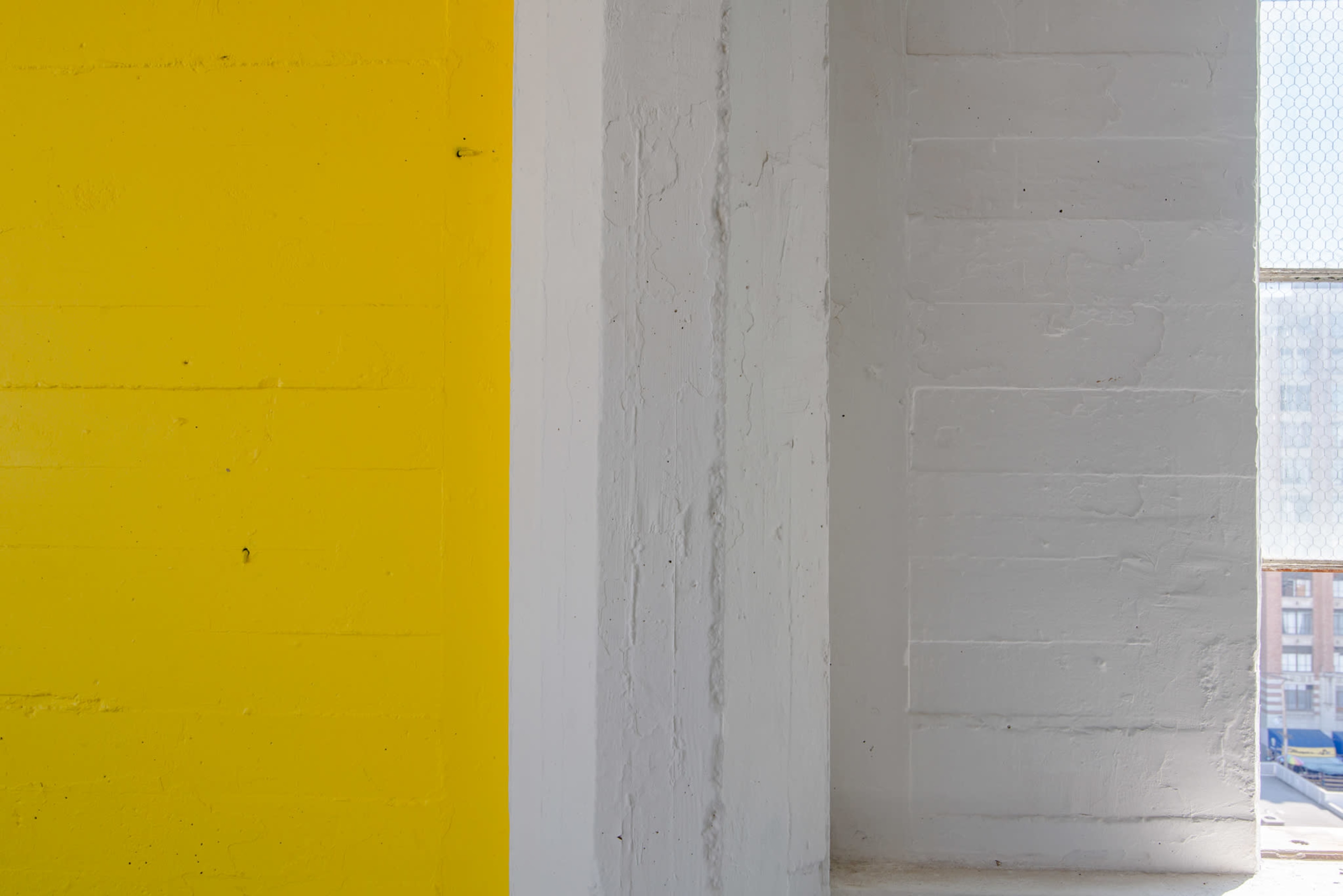 The image shows a section of a wall painted in bright yellow adjacent to a white wall, with a window providing light on one side.