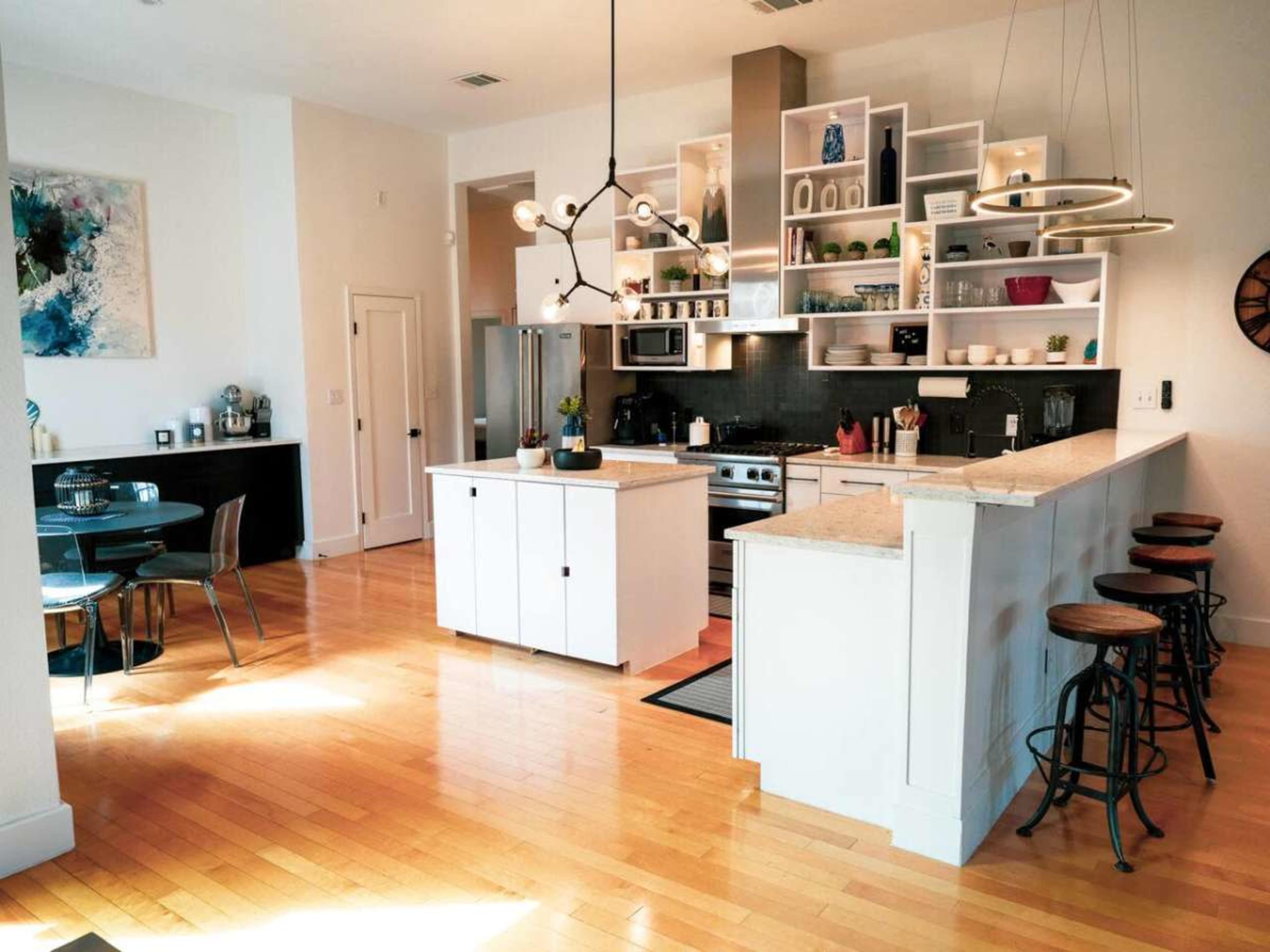 The image shows a modern kitchen with white cabinetry, an island with bar stools, and a dining area featuring a black table.