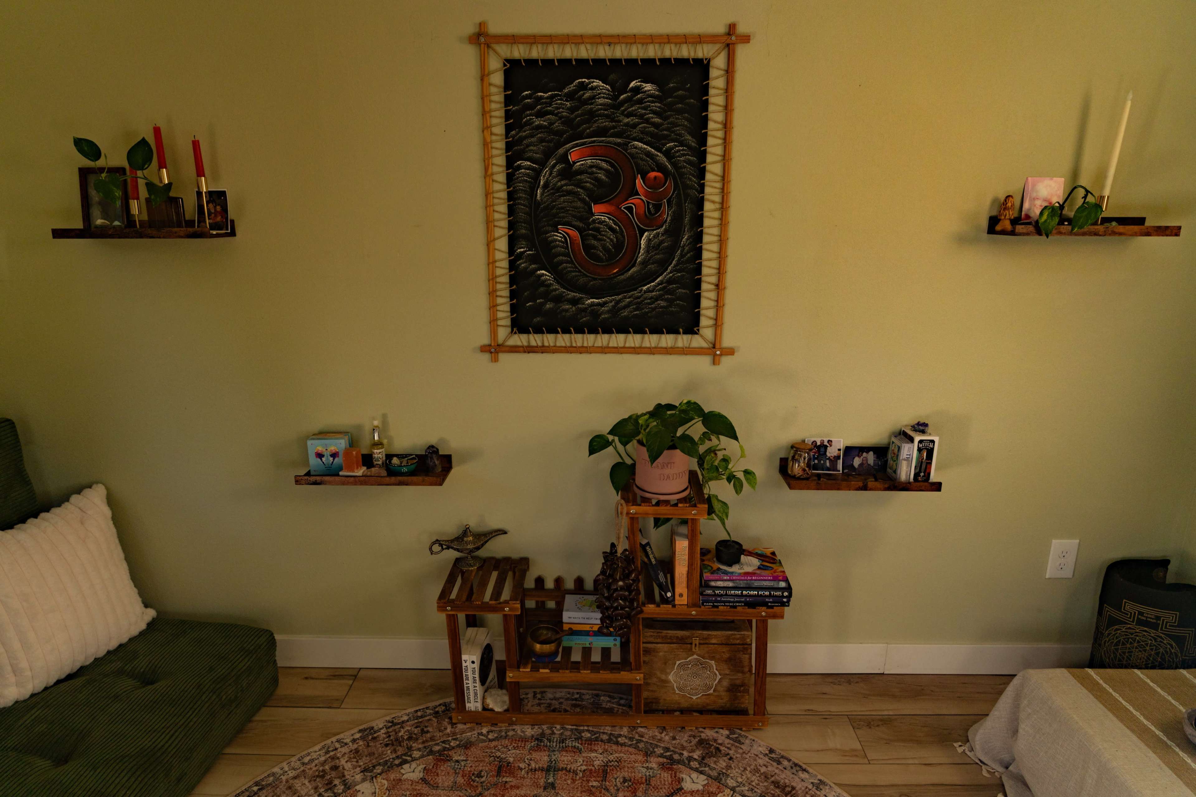 The image shows a cozy interior with bamboo shelves displaying decorative items, a green couch, and a large wall art piece featuring a symbol on a light green wall.