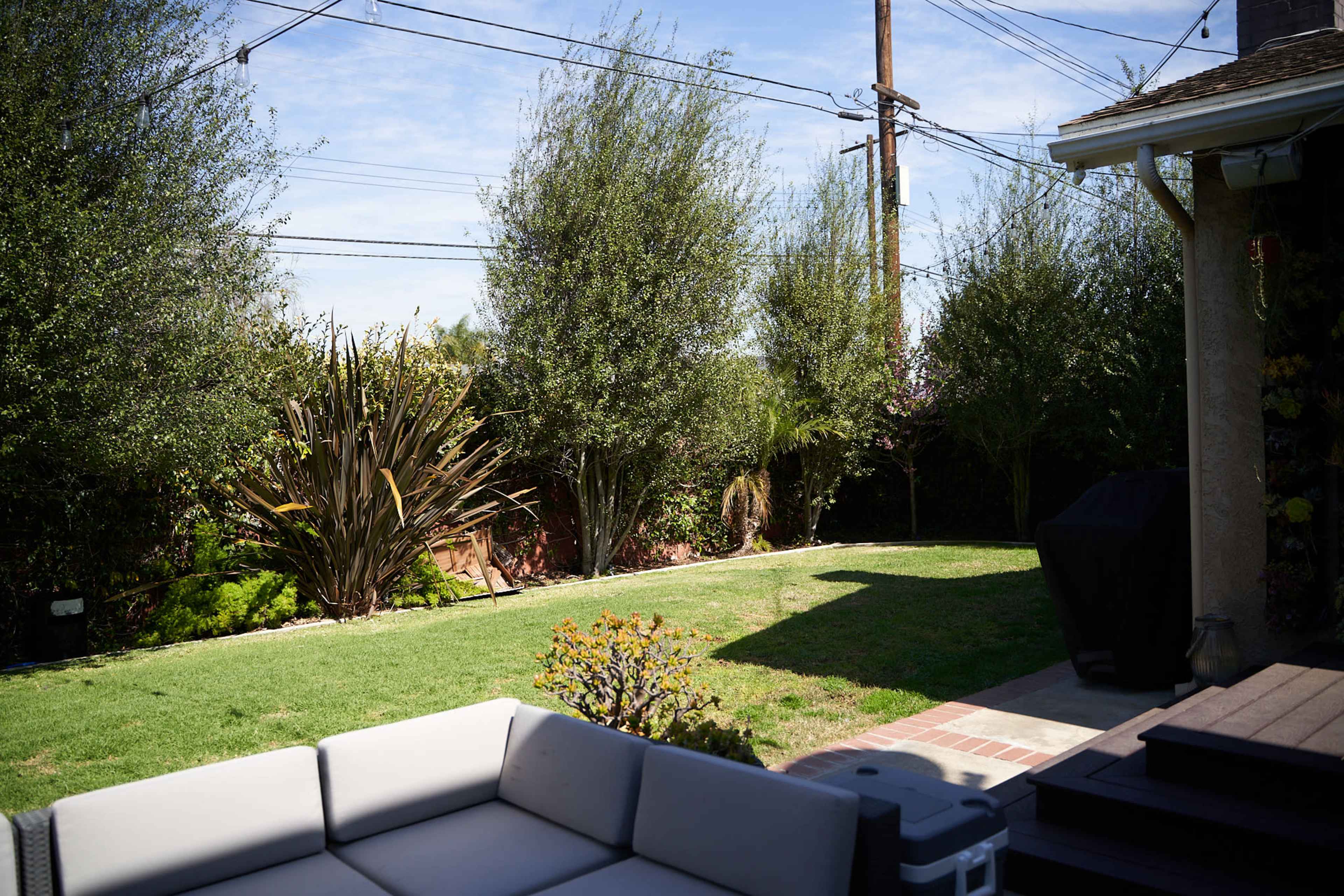 A backyard scene features a grassy area bordered by trees and shrubs, with patio furniture in the foreground.