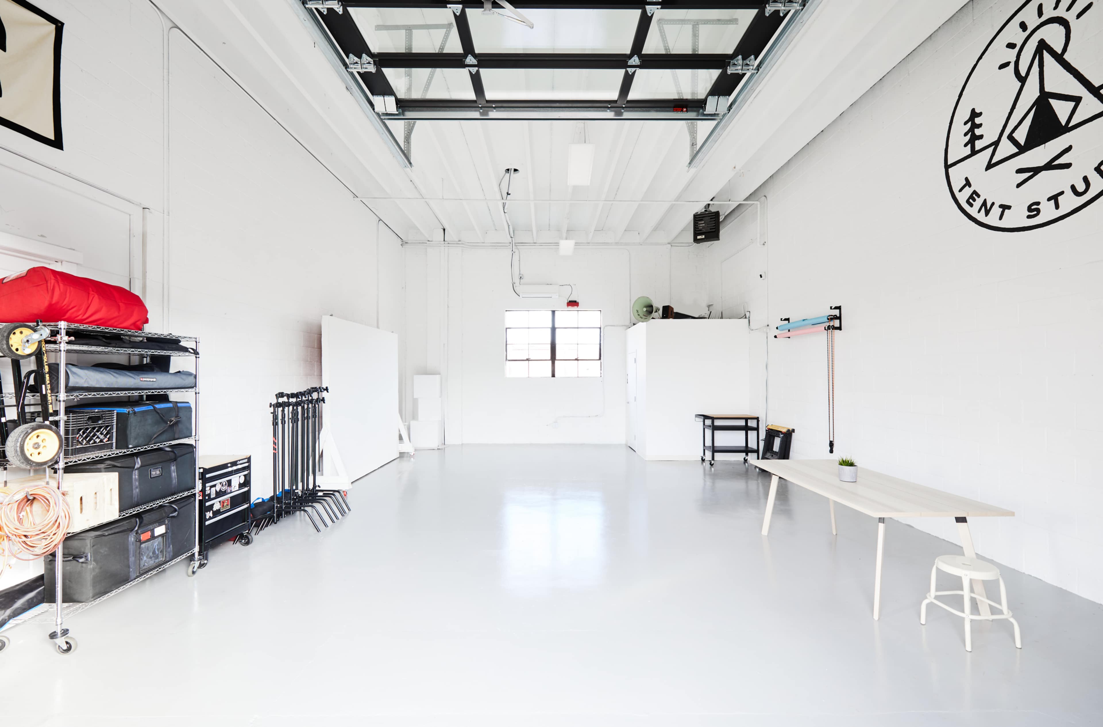 A spacious, well-lit studio with white walls, a polished floor, and minimal furniture including a table and storage units along one side.