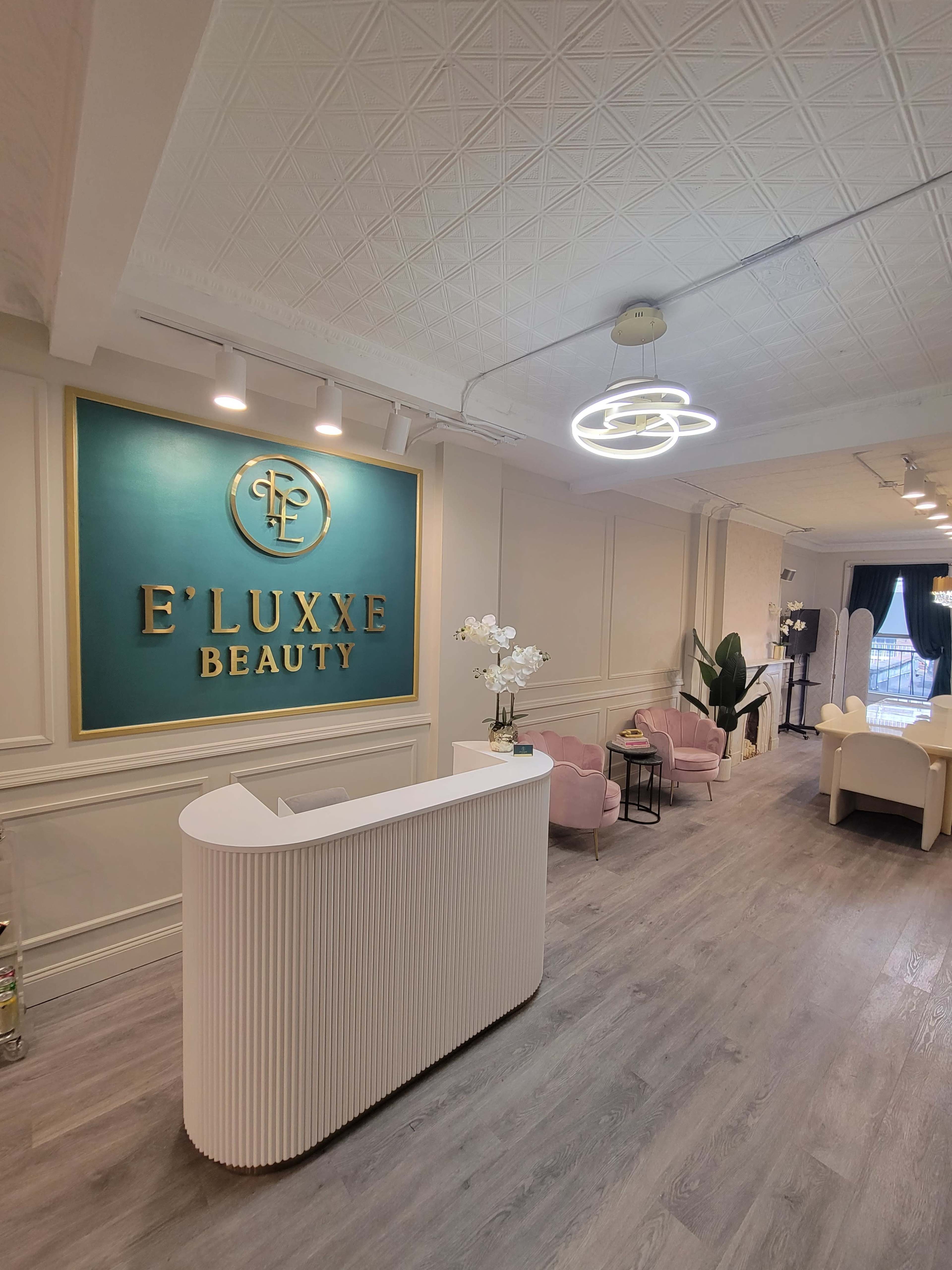 The image shows a modern beauty salon reception area featuring a white curved desk, pink chairs, and decorative elements on the walls.