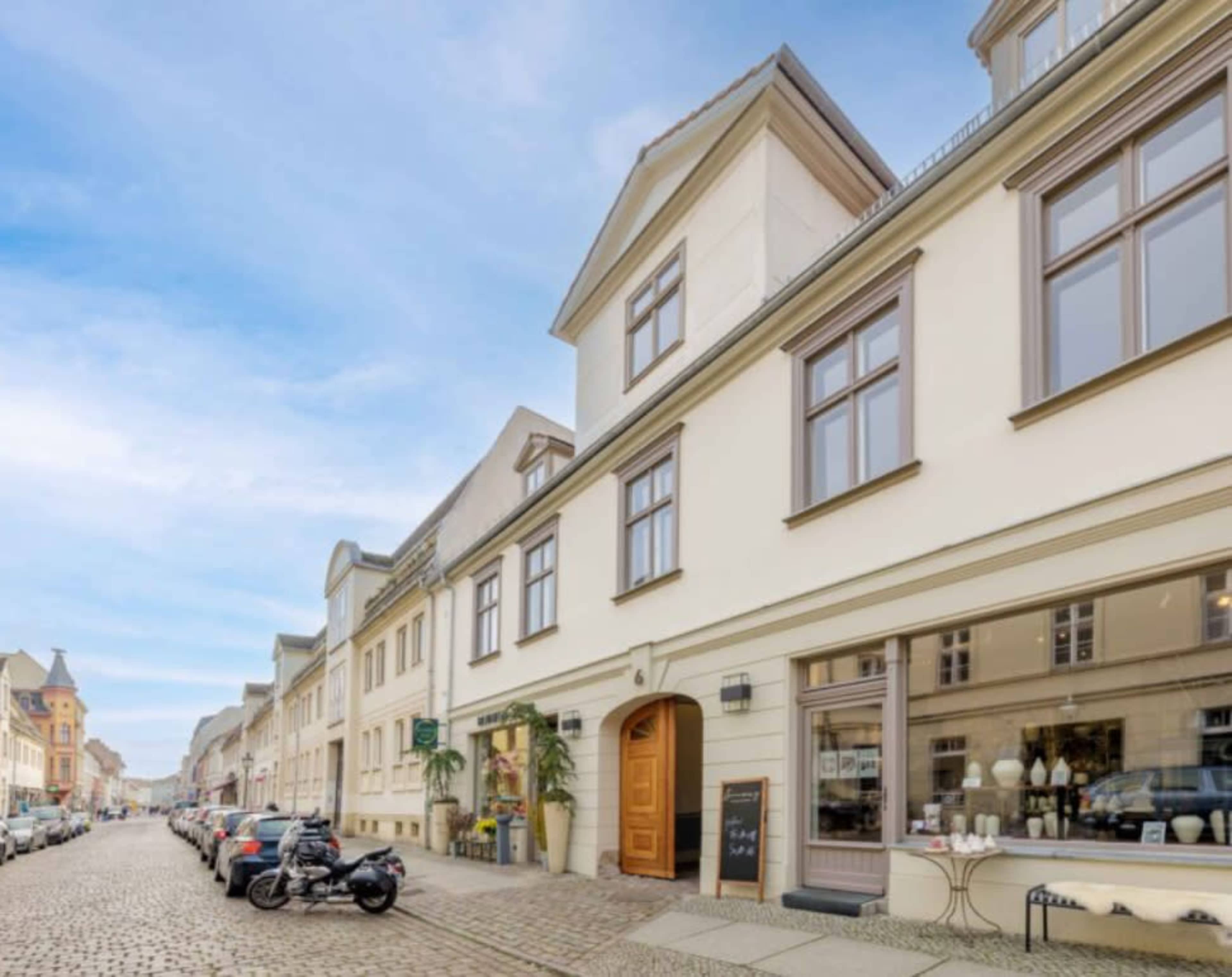 A cobblestone street is lined with buildings, featuring a mix of shops and parked vehicles.