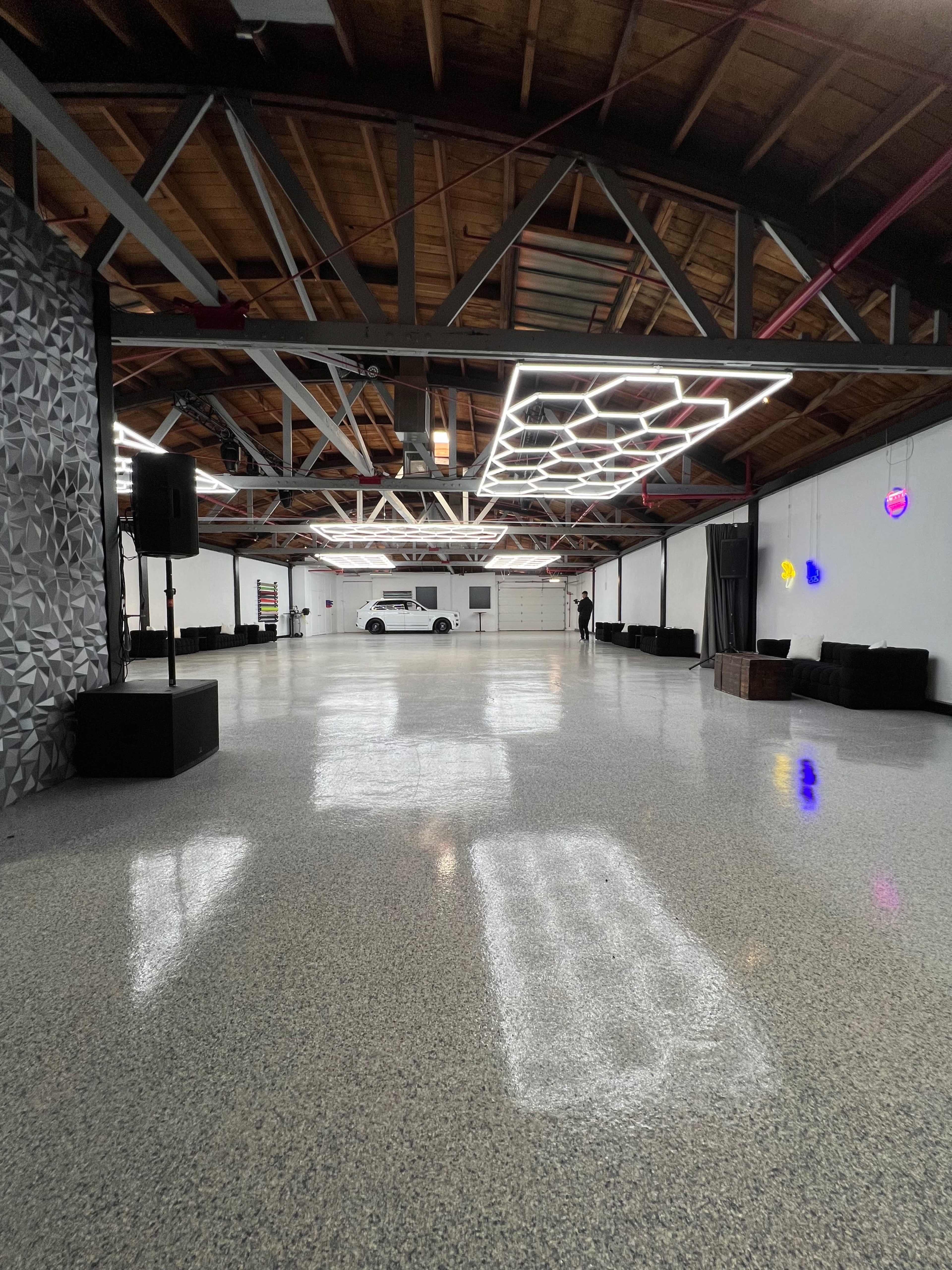 A spacious, well-lit indoor venue with polished concrete flooring, featuring modern lighting fixtures and minimal furnishings.