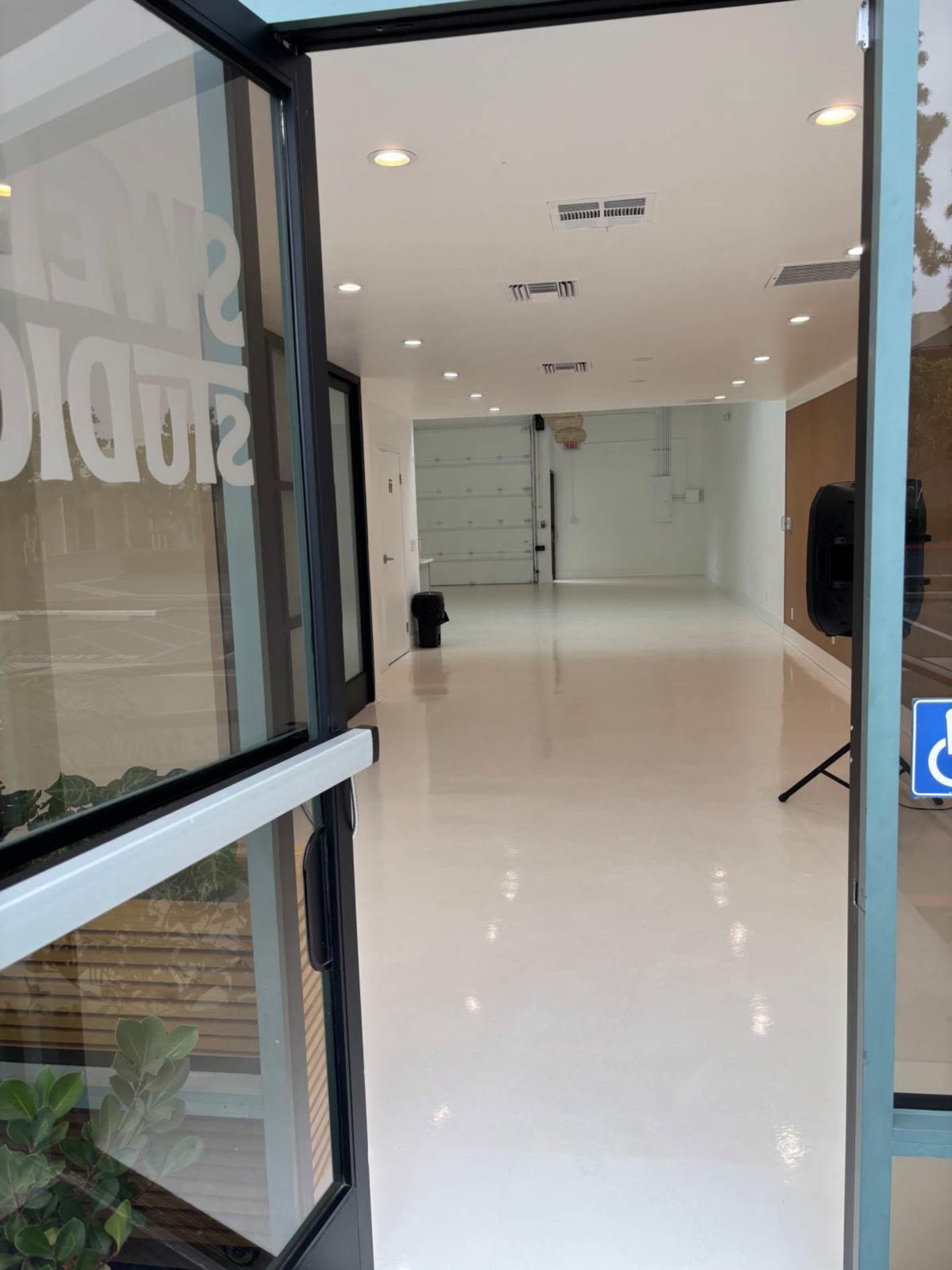 The image shows the entrance of a vacant studio with a clean, polished floor and white walls, visible through an open glass door.