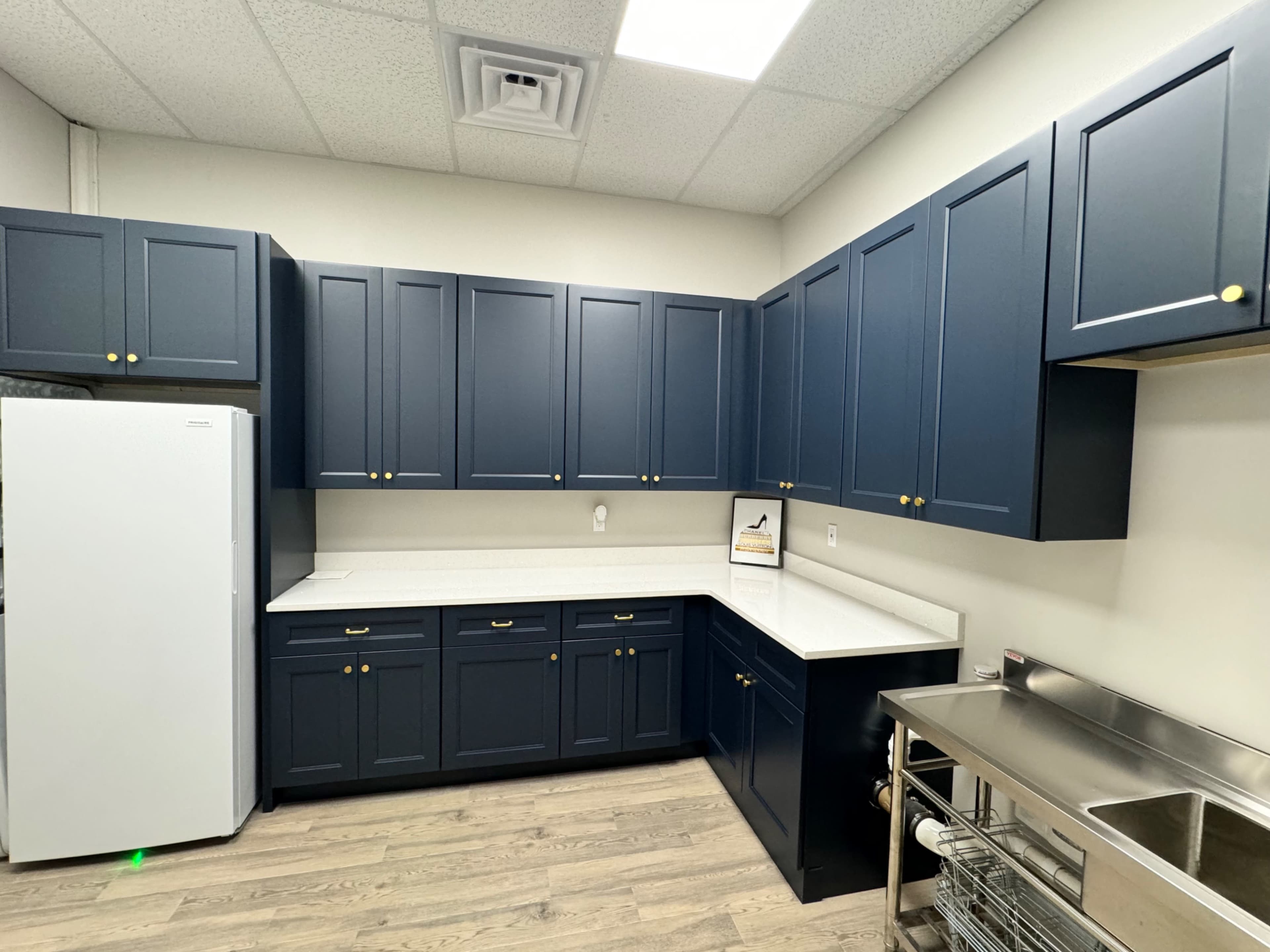 A kitchen with navy blue cabinets, a white refrigerator, and a stainless steel countertop.