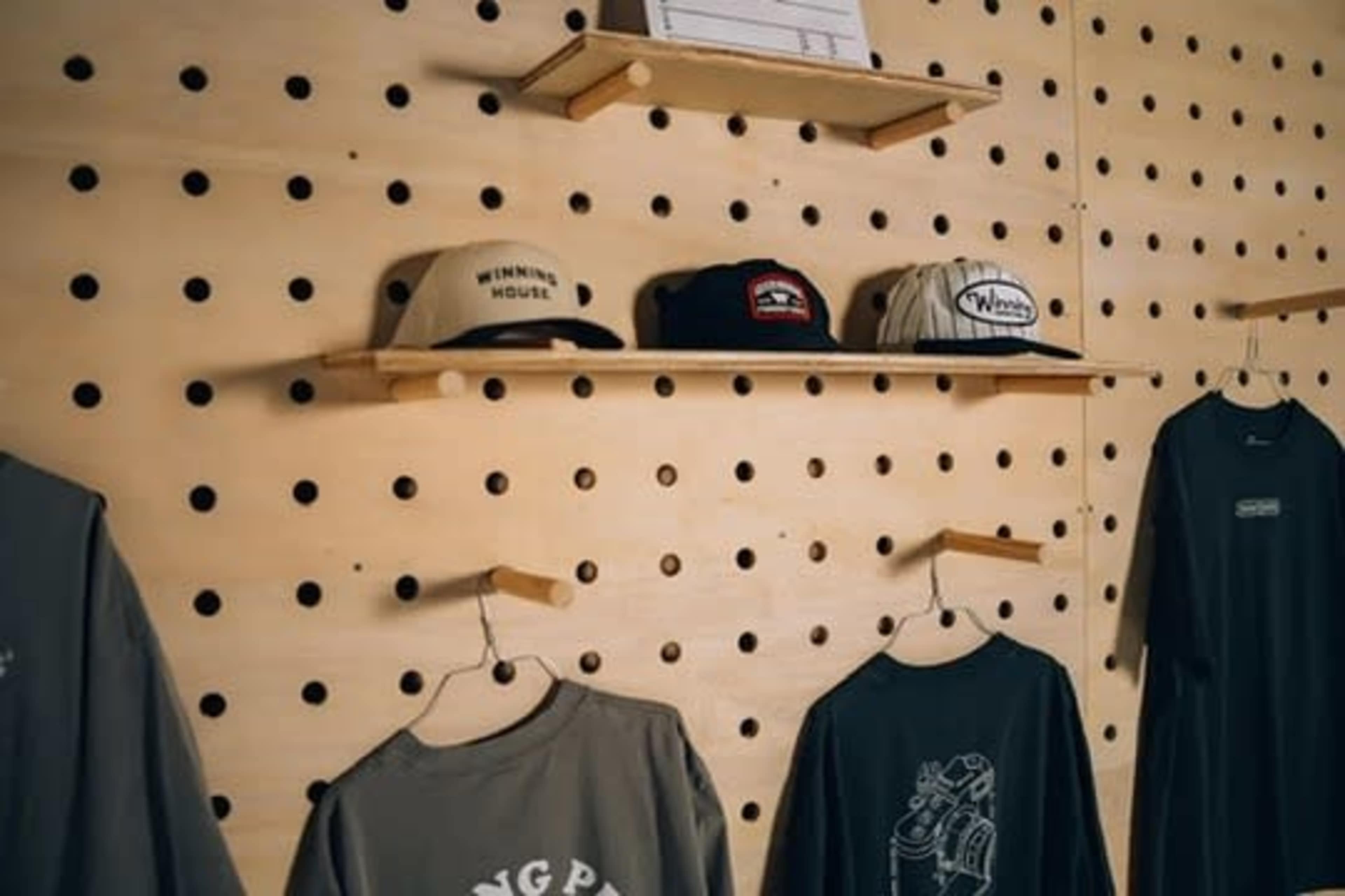 The image shows a wall with a pegboard displaying caps on shelves and T-shirts hanging below.