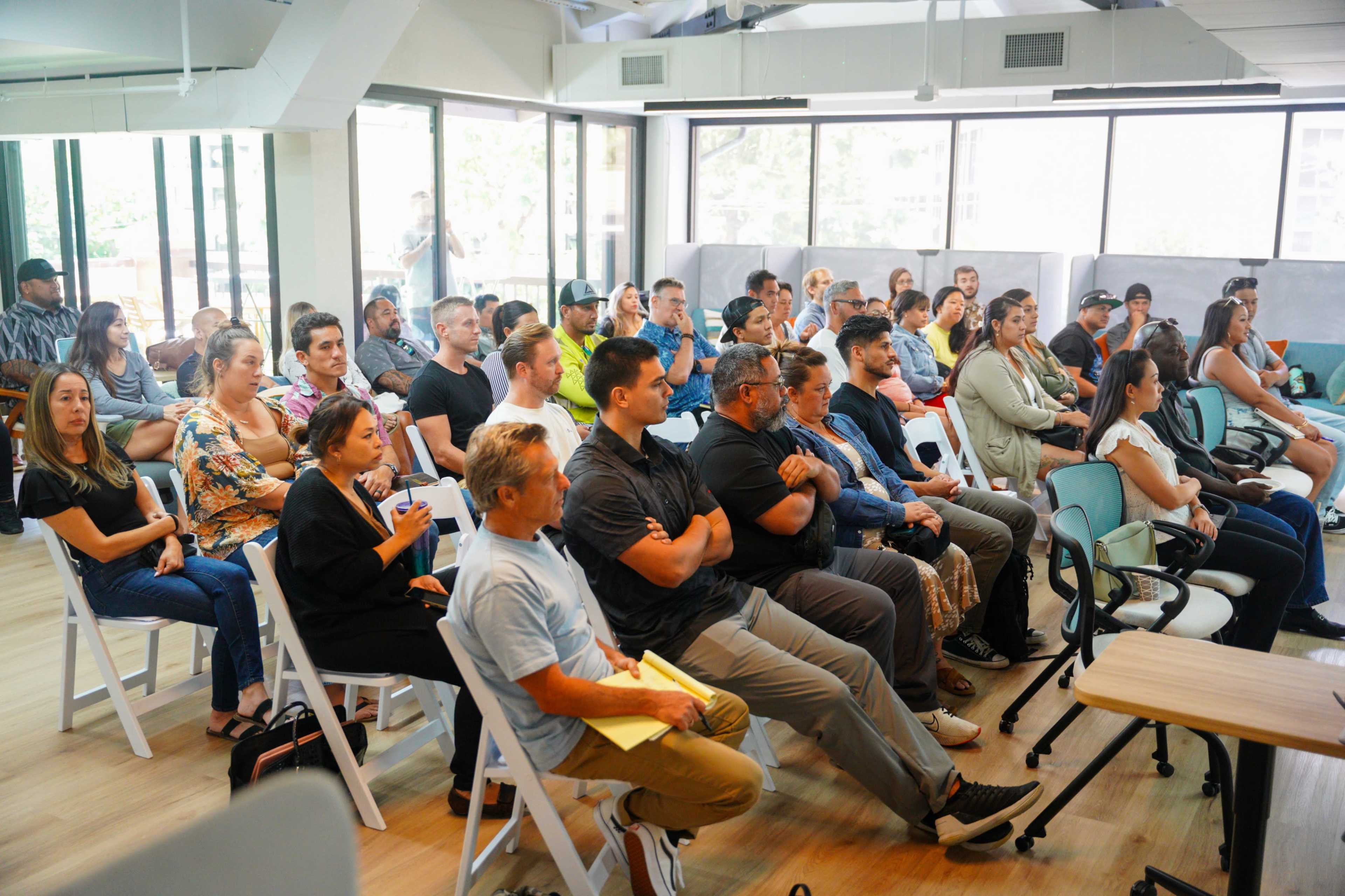 A diverse group of people are seated in a modern conference room, attentively facing a speaker at the front.