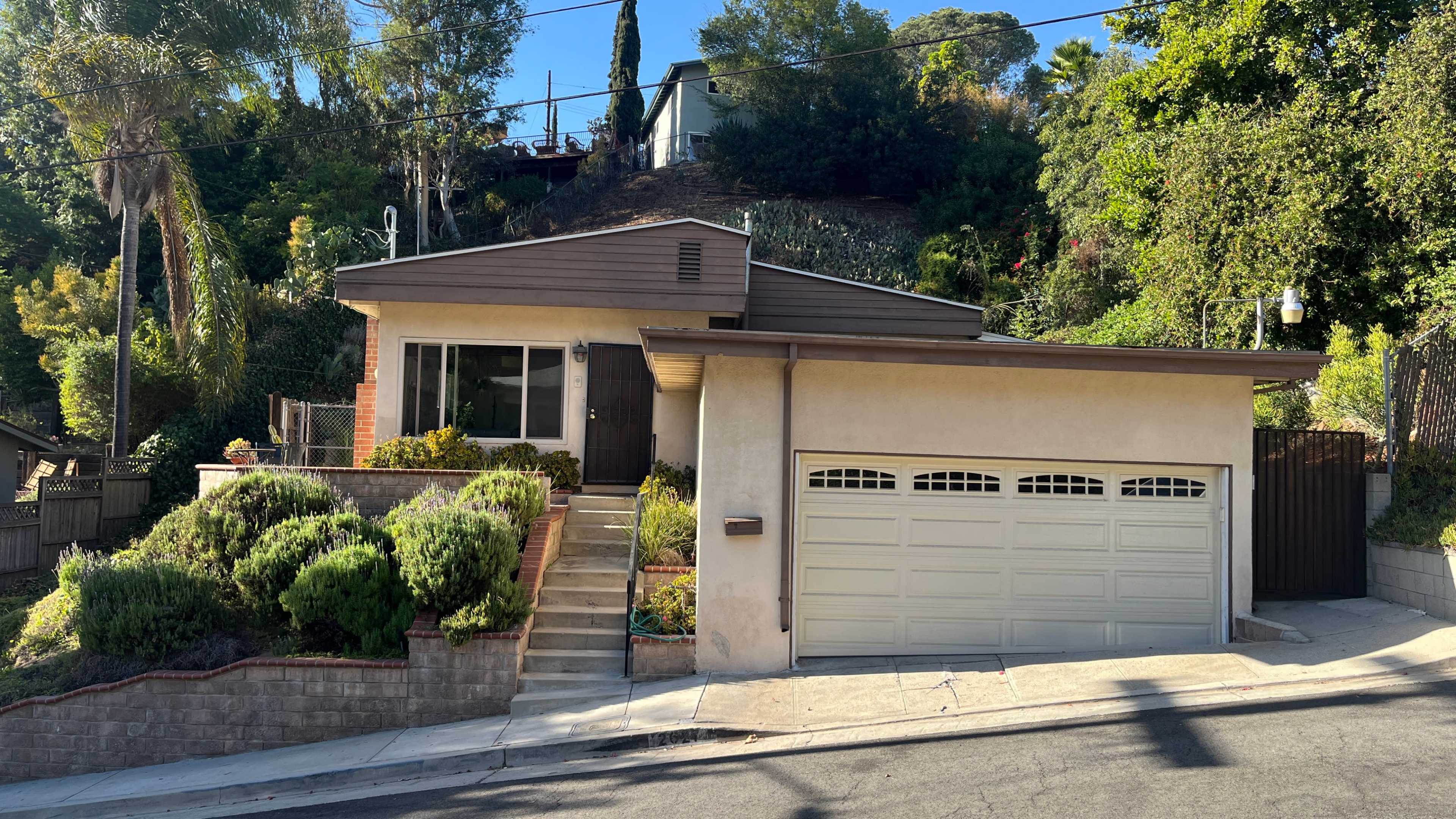 The image shows a single-story house with a garage and landscaped front yard, situated on a hillside.