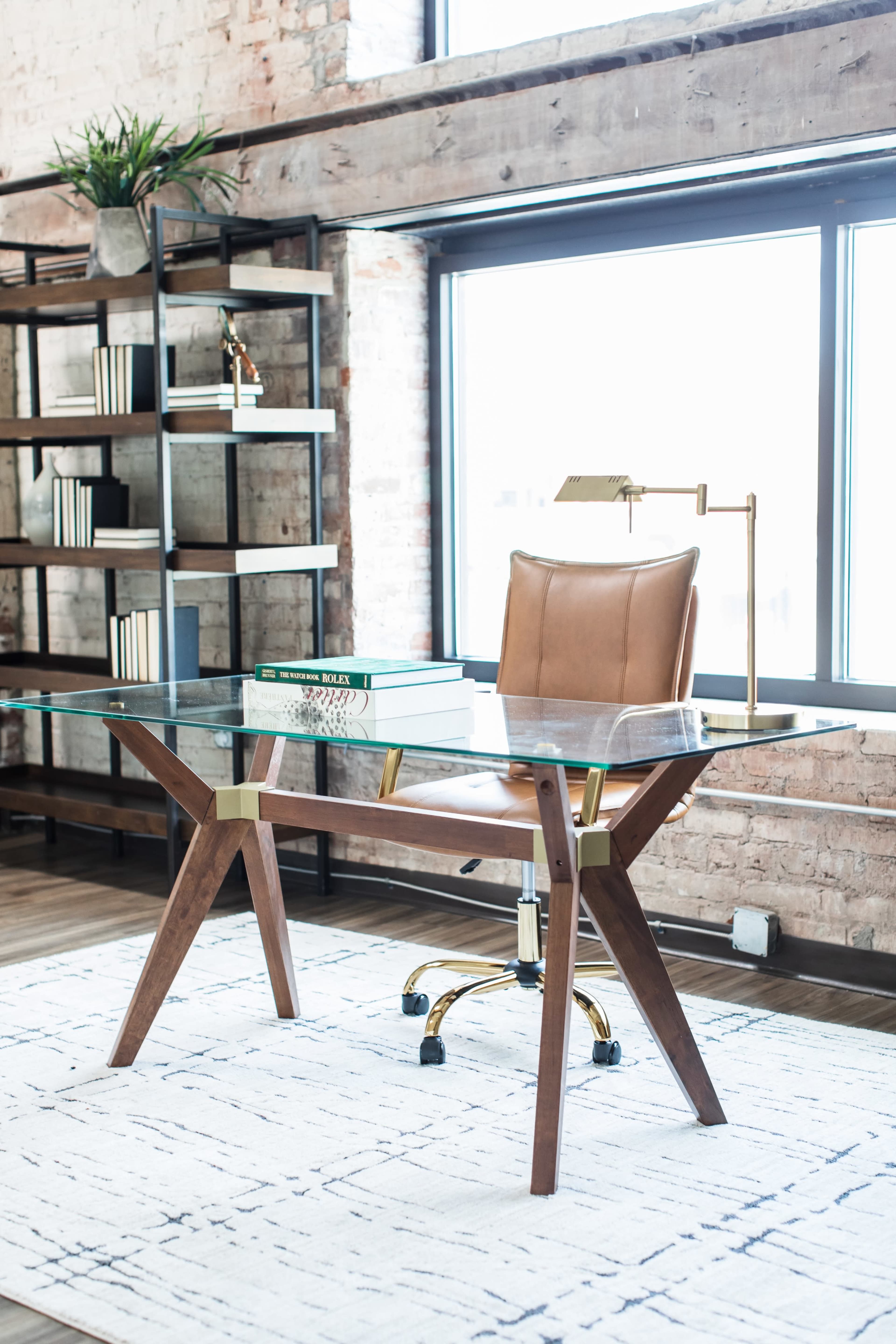 The image features a modern office setup with a glass-top desk, a leather chair on a rolling base, and a bookshelf filled with books.