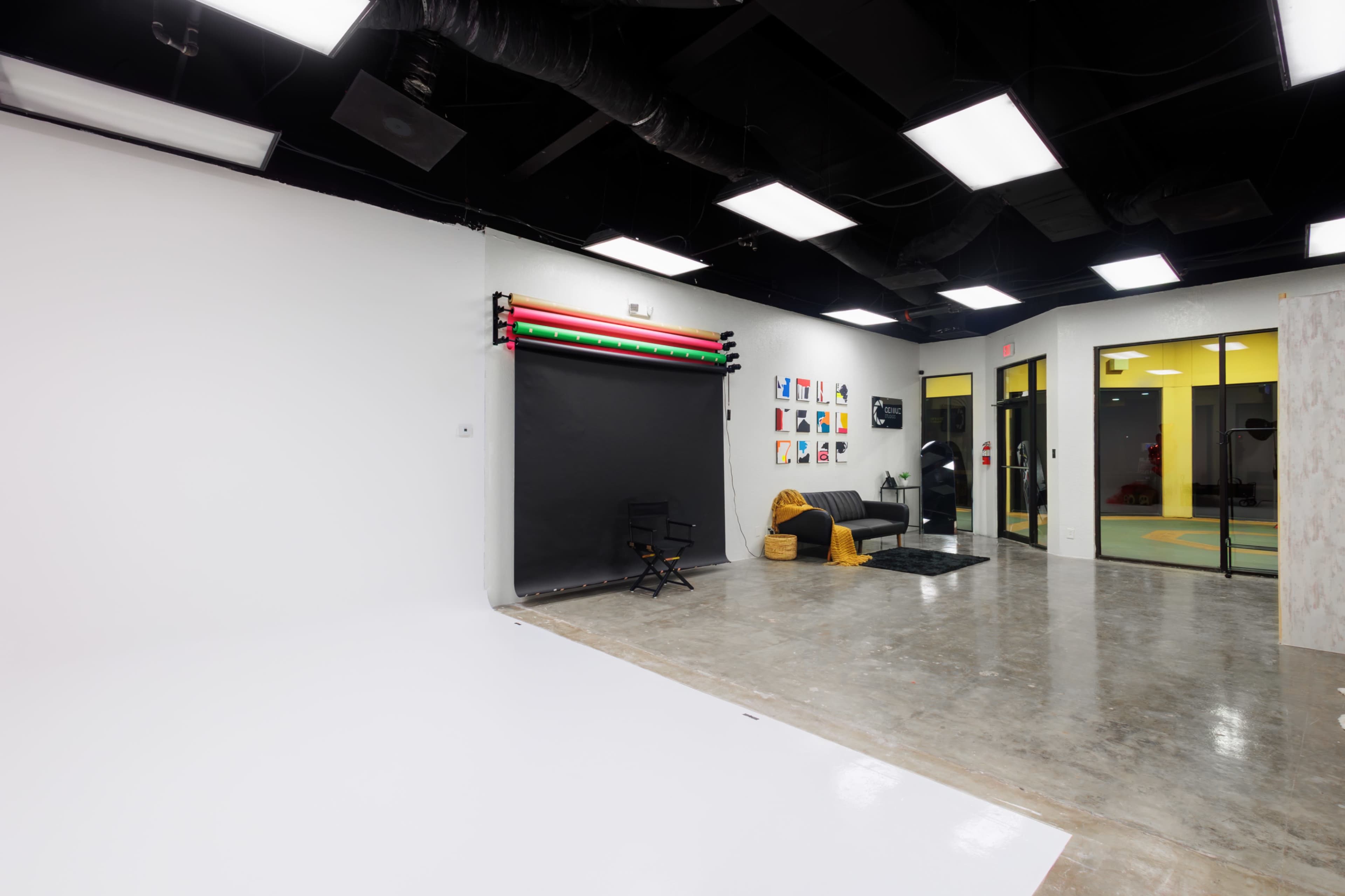 A spacious photography studio with a black backdrop, a seating area, and various colorful artworks displayed on the wall.