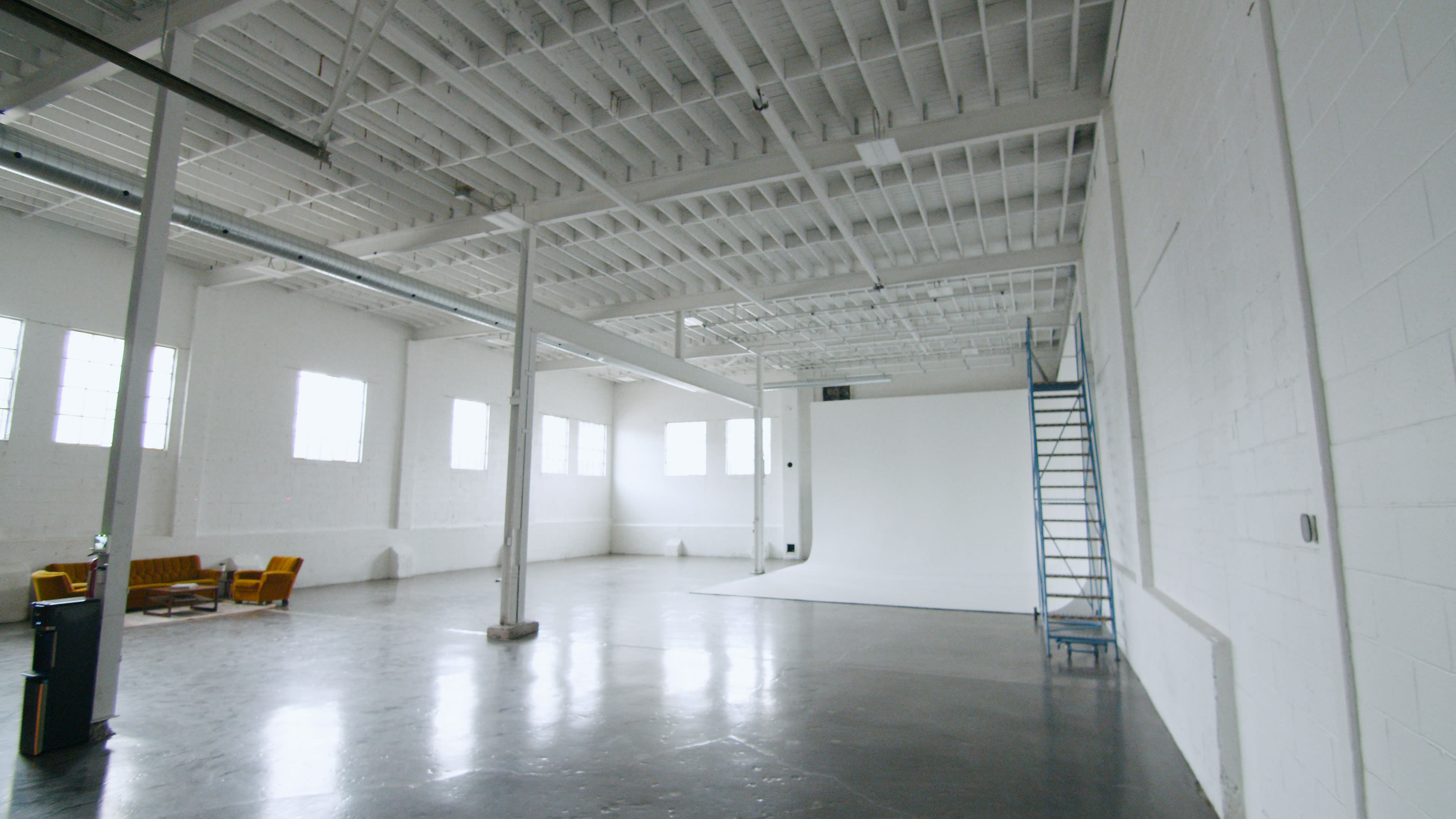 A spacious, empty studio with high white walls, large windows, and a concrete floor.