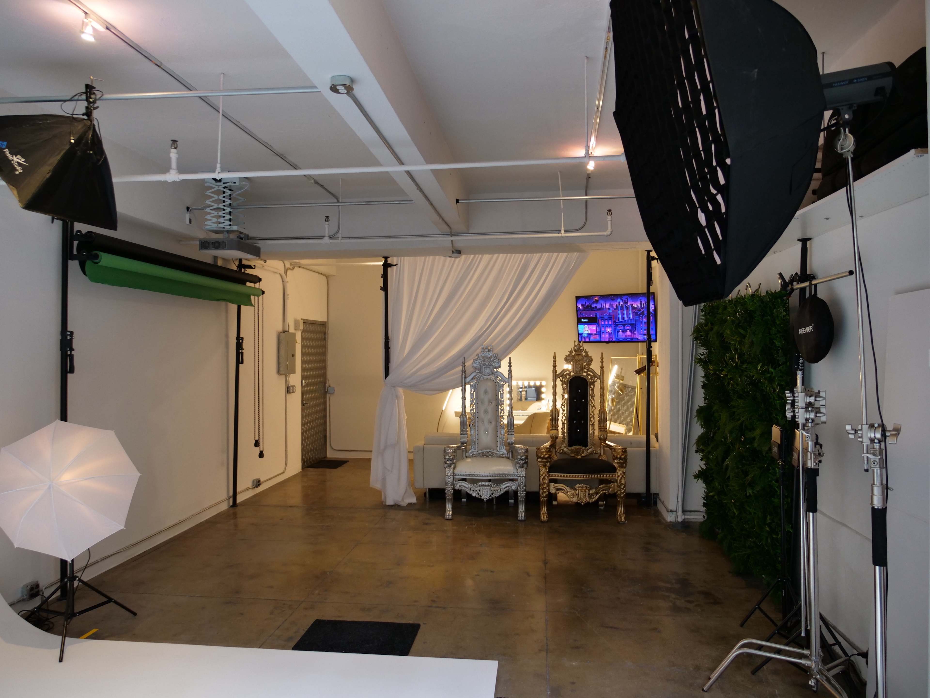 A photography studio featuring two ornate chairs, soft lighting, and various photography equipment set up in a spacious area.