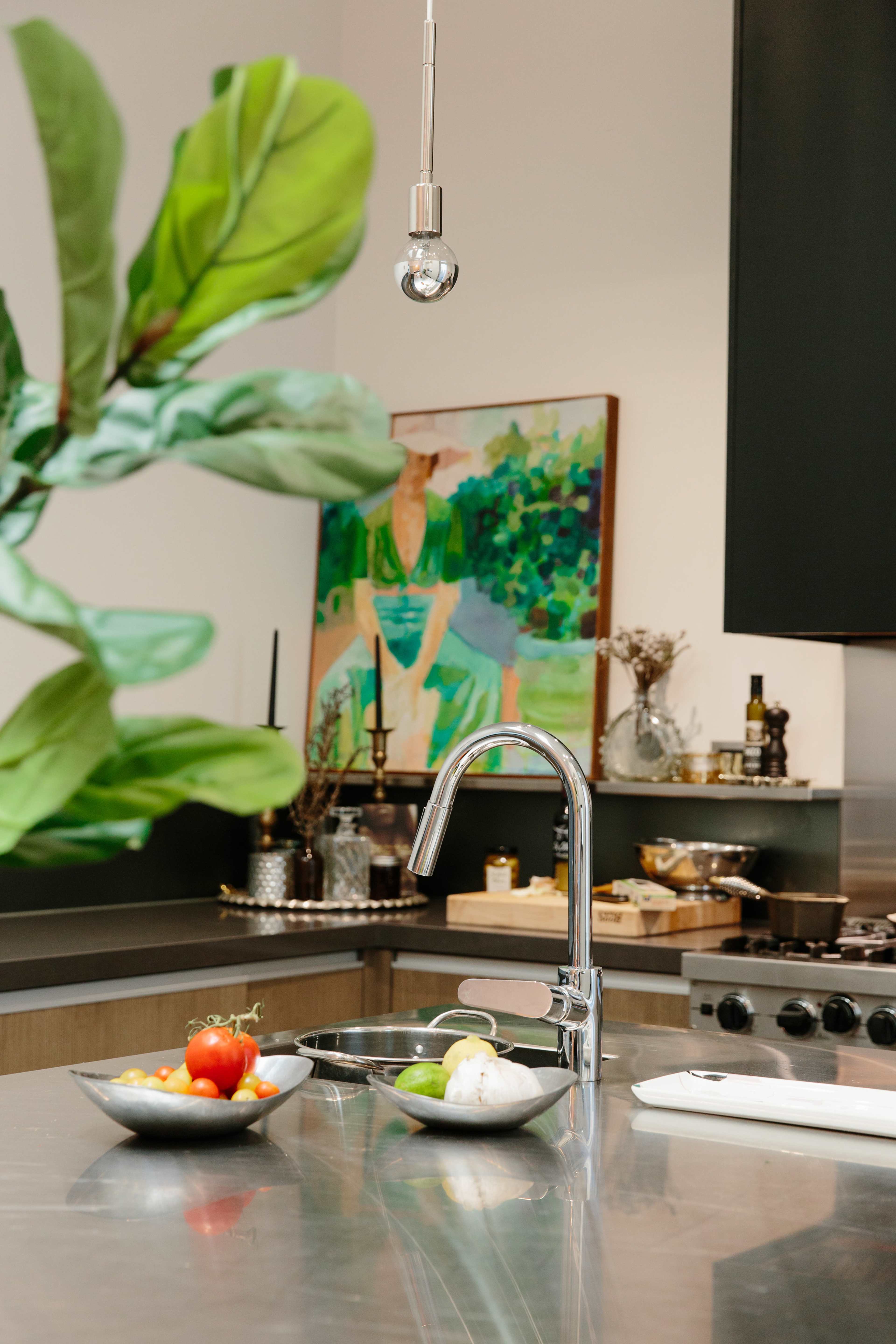 A modern kitchen featuring a stainless steel countertop, a contemporary faucet, and bowls of fresh vegetables beside an abstract painting on the wall.