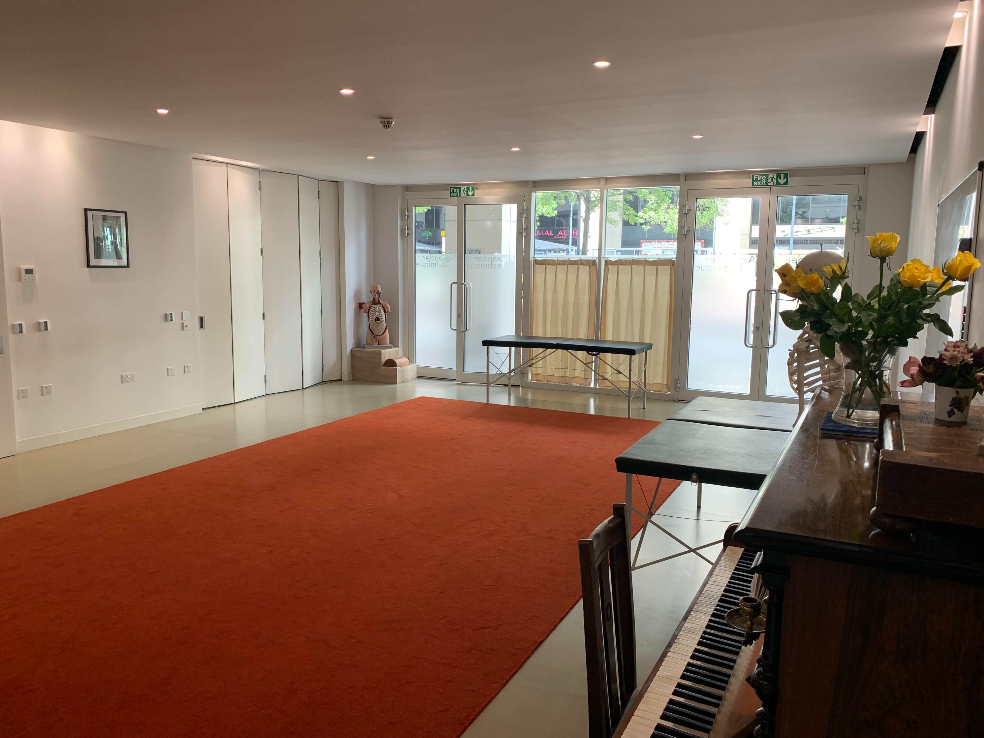 The scene shows a spacious room with a large orange carpet, a wooden piano, a table in the background, and large glass doors leading outside.