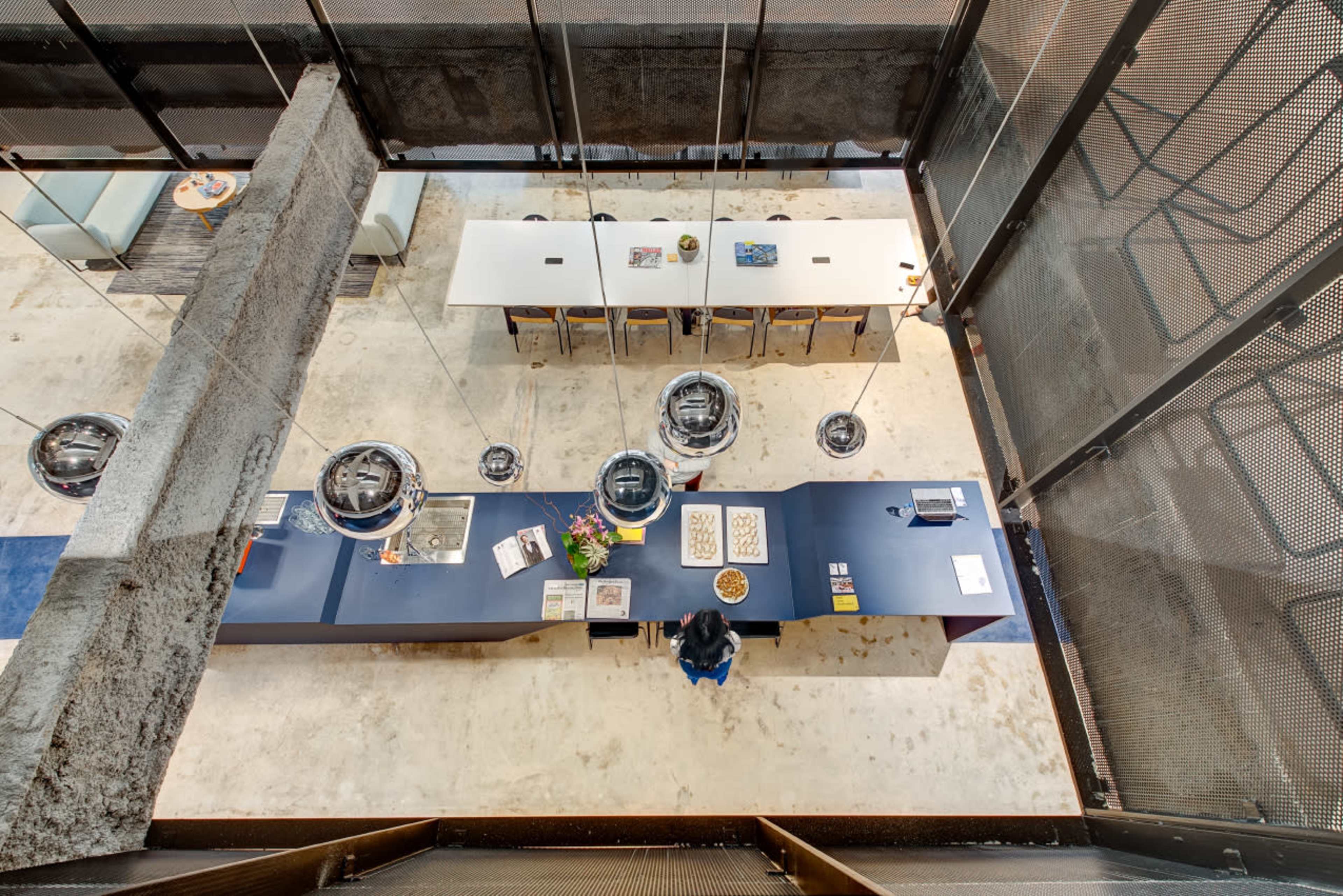 A modern office interior with a central reception desk, surrounded by tables and chairs, under a multi-level architectural design.