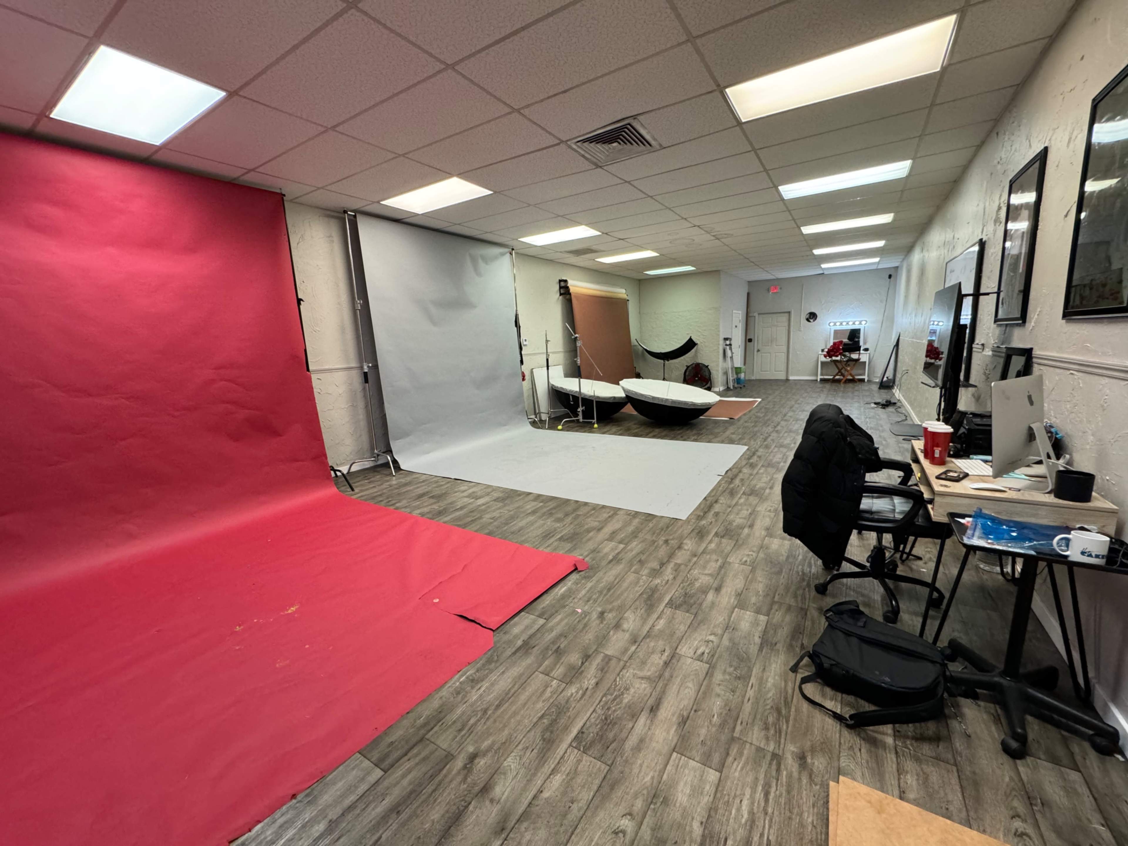 A photography studio with a red backdrop, a gray backdrop, a hanging backdrop, a large white surface, and various equipment arranged around a workspace.