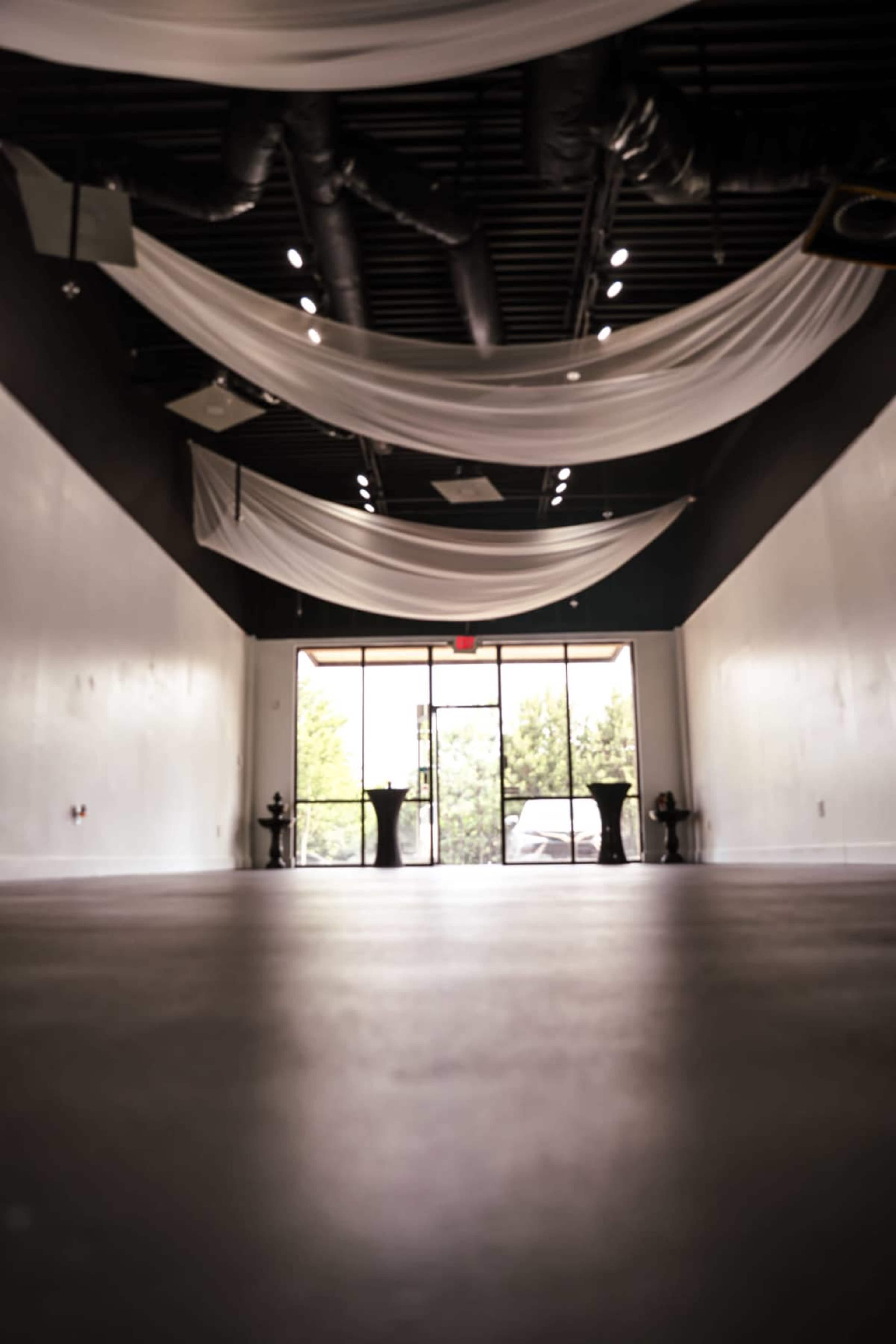 The image shows an empty event space with a smooth floor and draped fabric overhead, leading to large windows at the front.