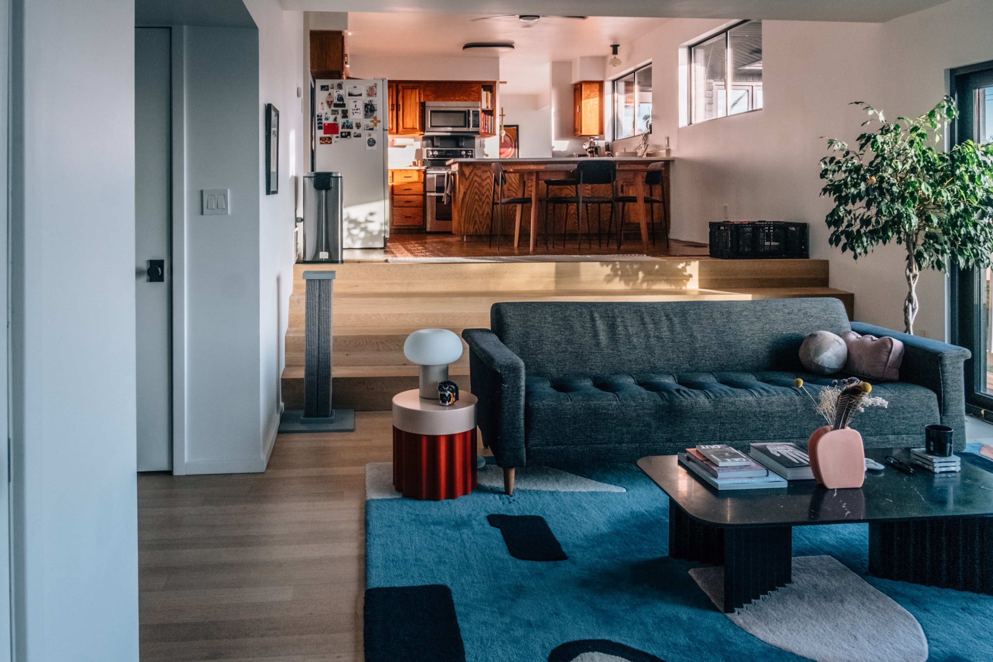 The image shows a modern living room with a sofa, a coffee table, and a dining area visible in the background.