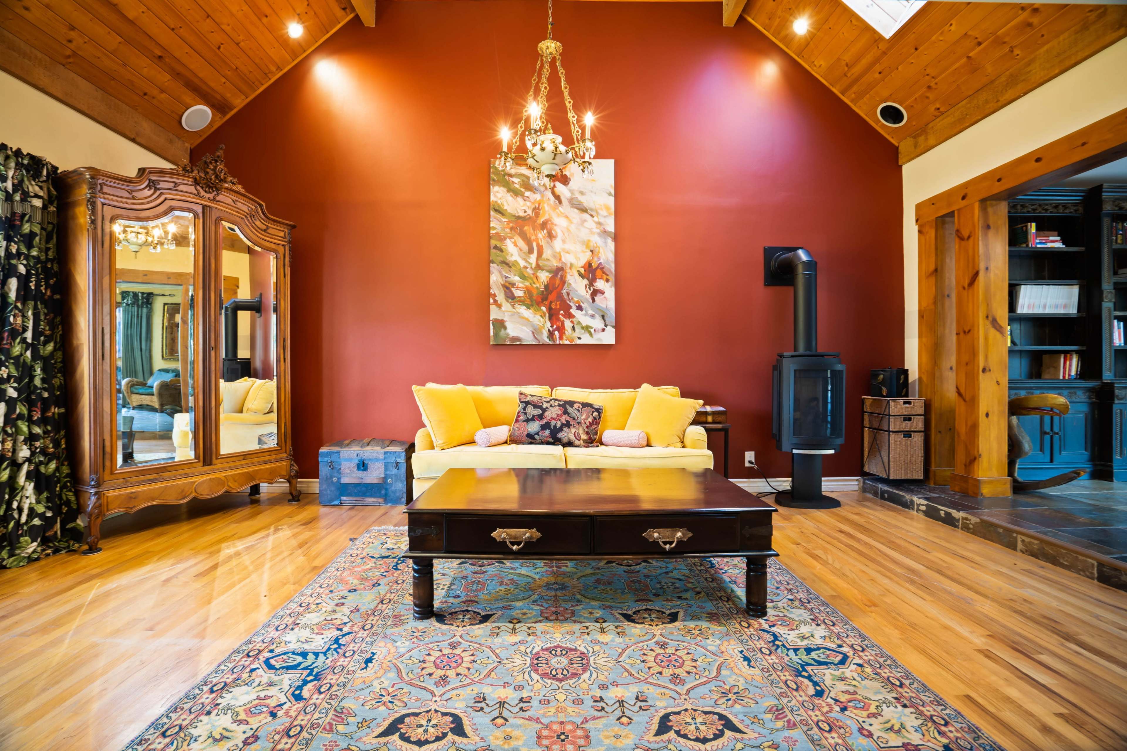 A cozy living room featuring a yellow sofa, a wooden coffee table, a decorative mirror, and a wall adorned with a colorful painting.