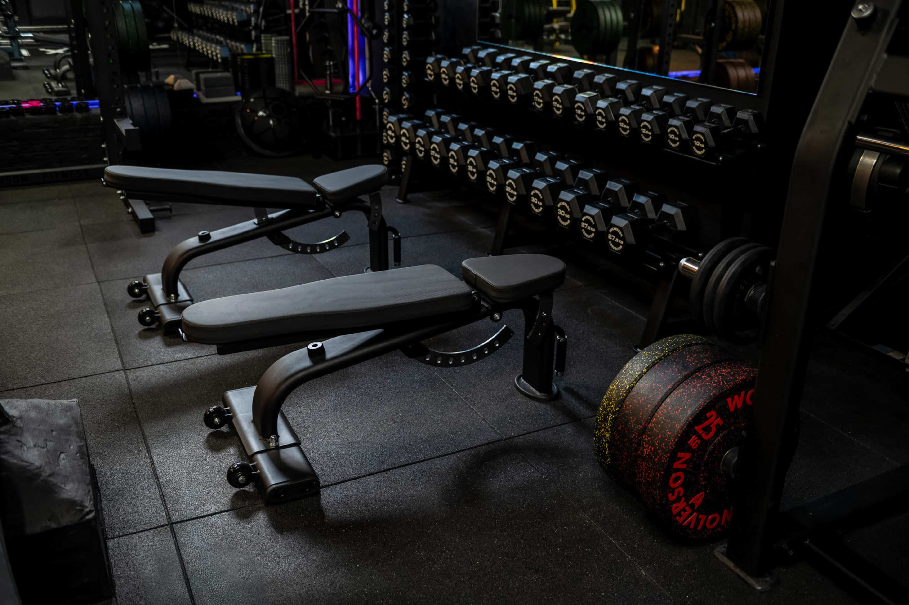 The image shows a well-equipped gym area featuring weight benches and a rack of weighted plates.