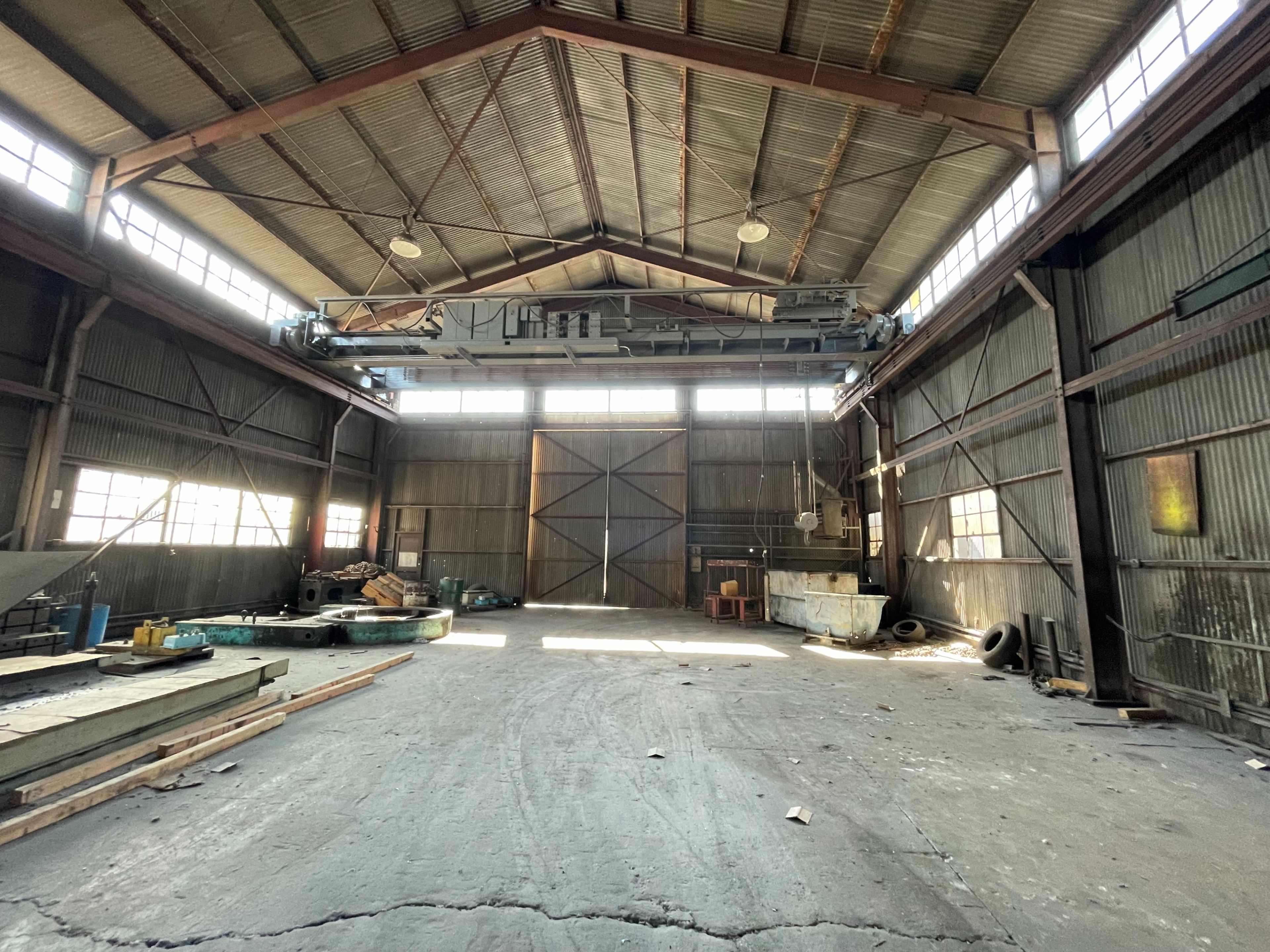 The interior of a large industrial warehouse features high ceilings, exposed beams, and scattered construction materials.