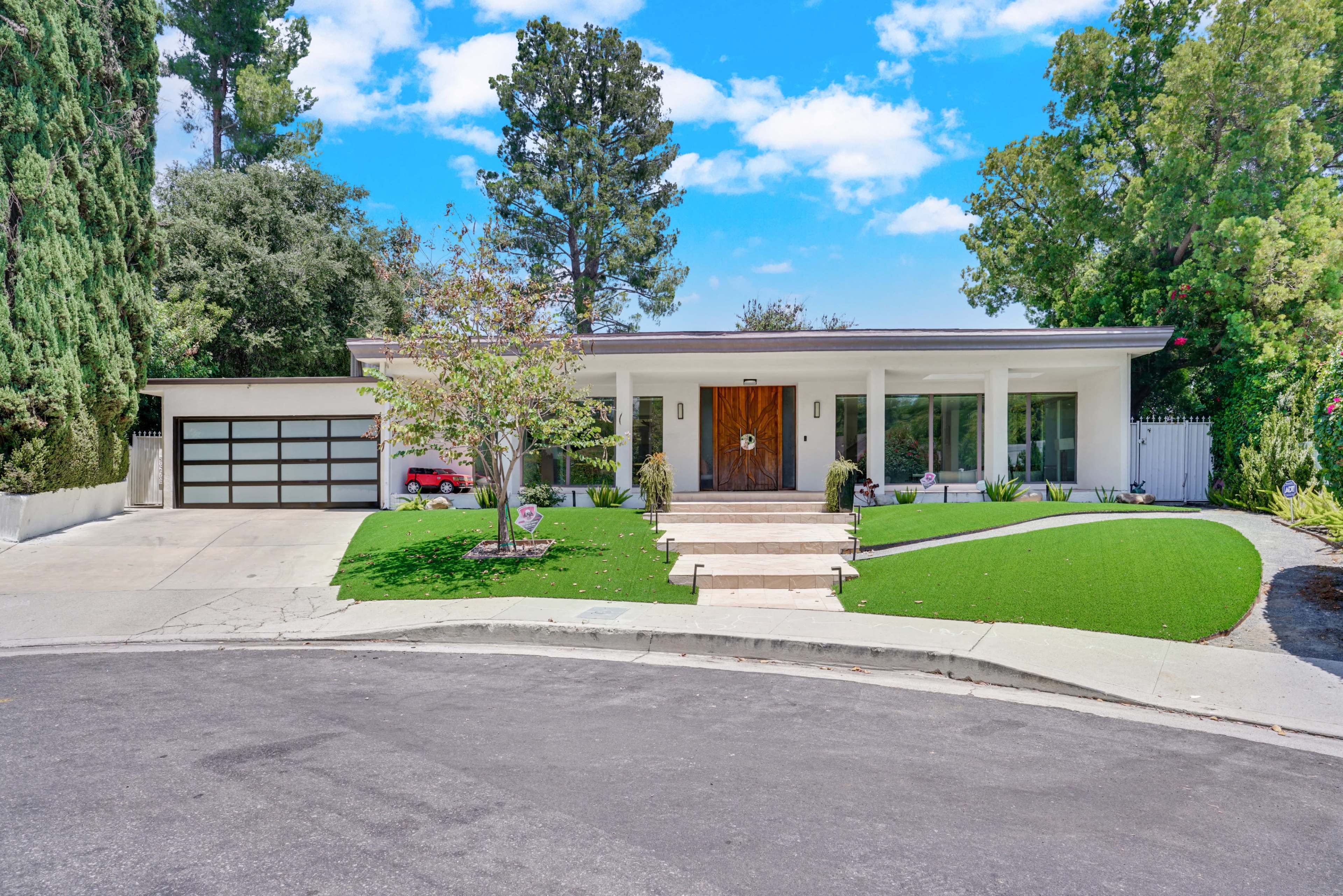 A modern, single-story house with a landscaped front yard and a circular driveway is situated at the end of a quiet street.