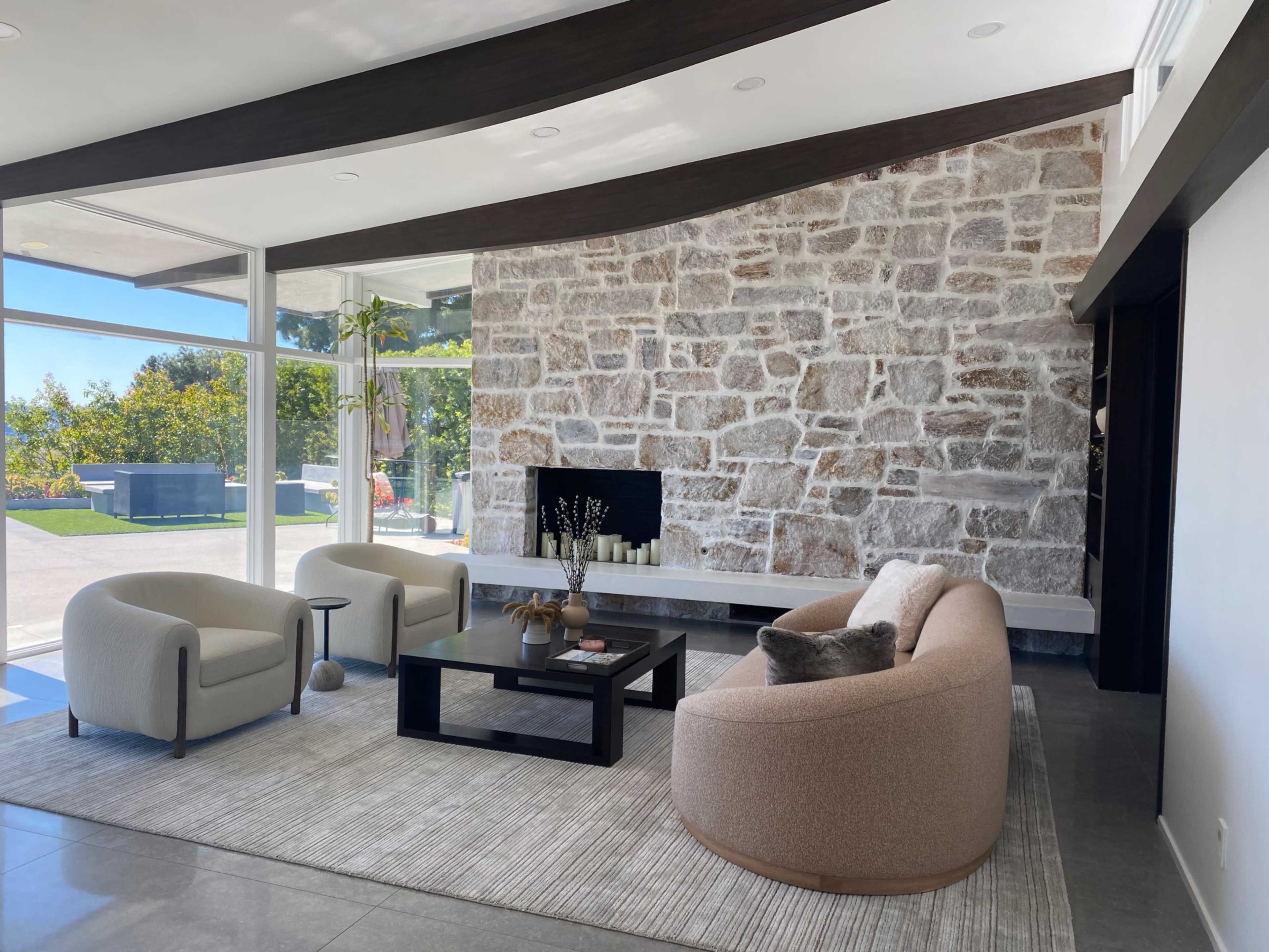 A modern living room with a stone accent wall, two curved sofas, a coffee table, and large windows providing natural light.