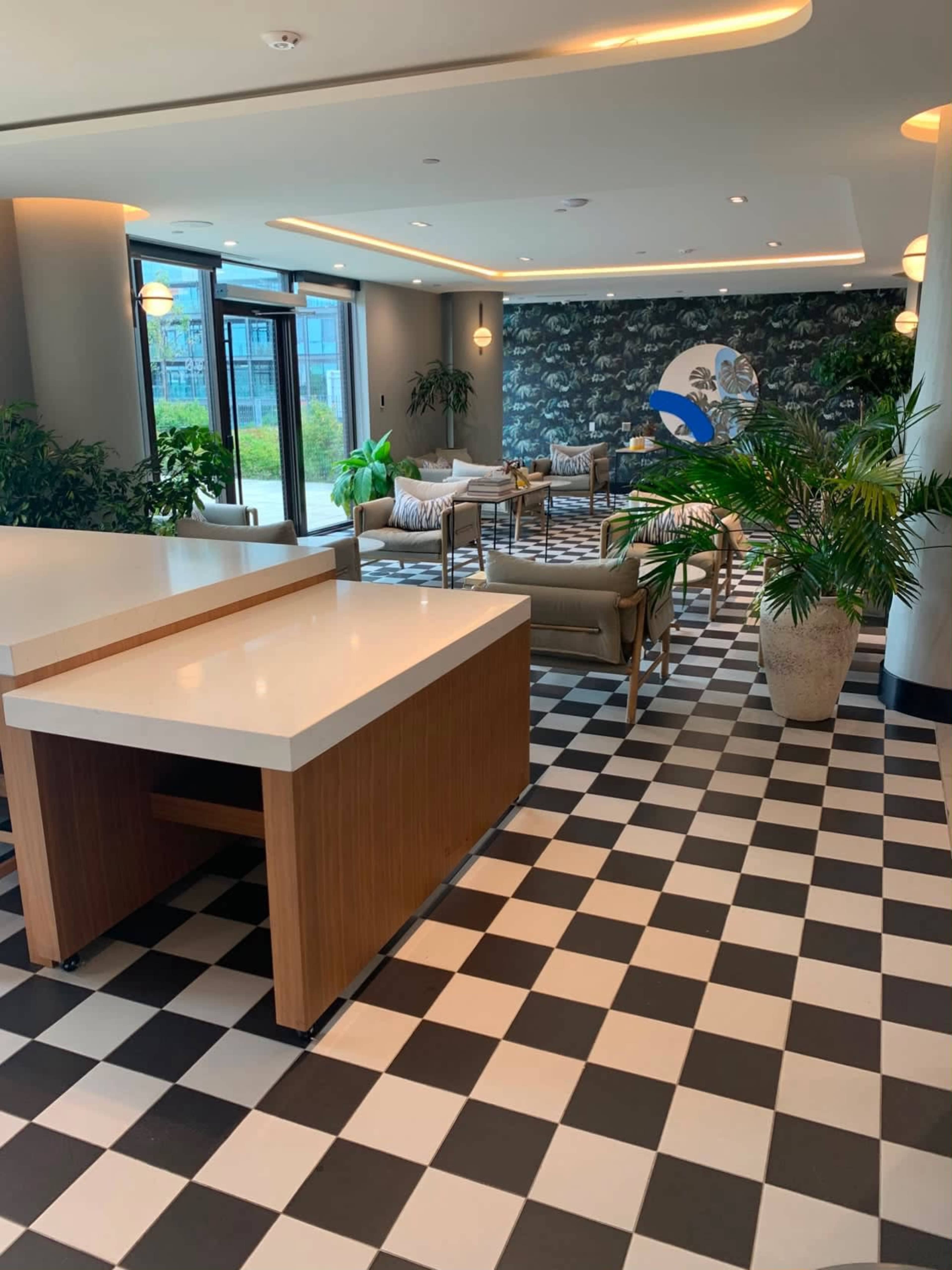The image shows a modern lounge area with a checkered floor, equipped with seating arrangements, plants, and artistic wall decor.