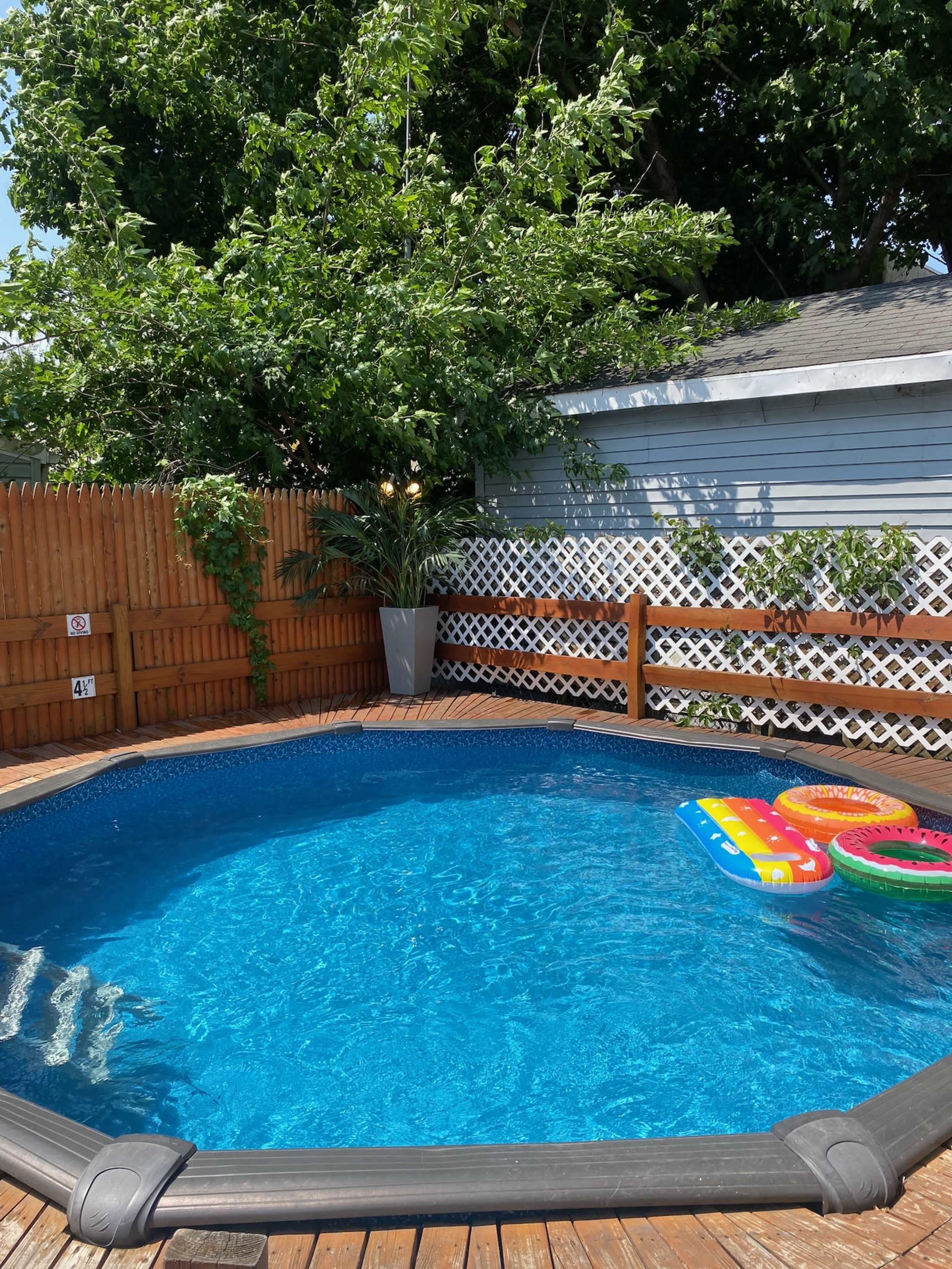 A rounded above-ground pool surrounded by a wooden deck, with colorful inflatable floats resting on the water's surface.