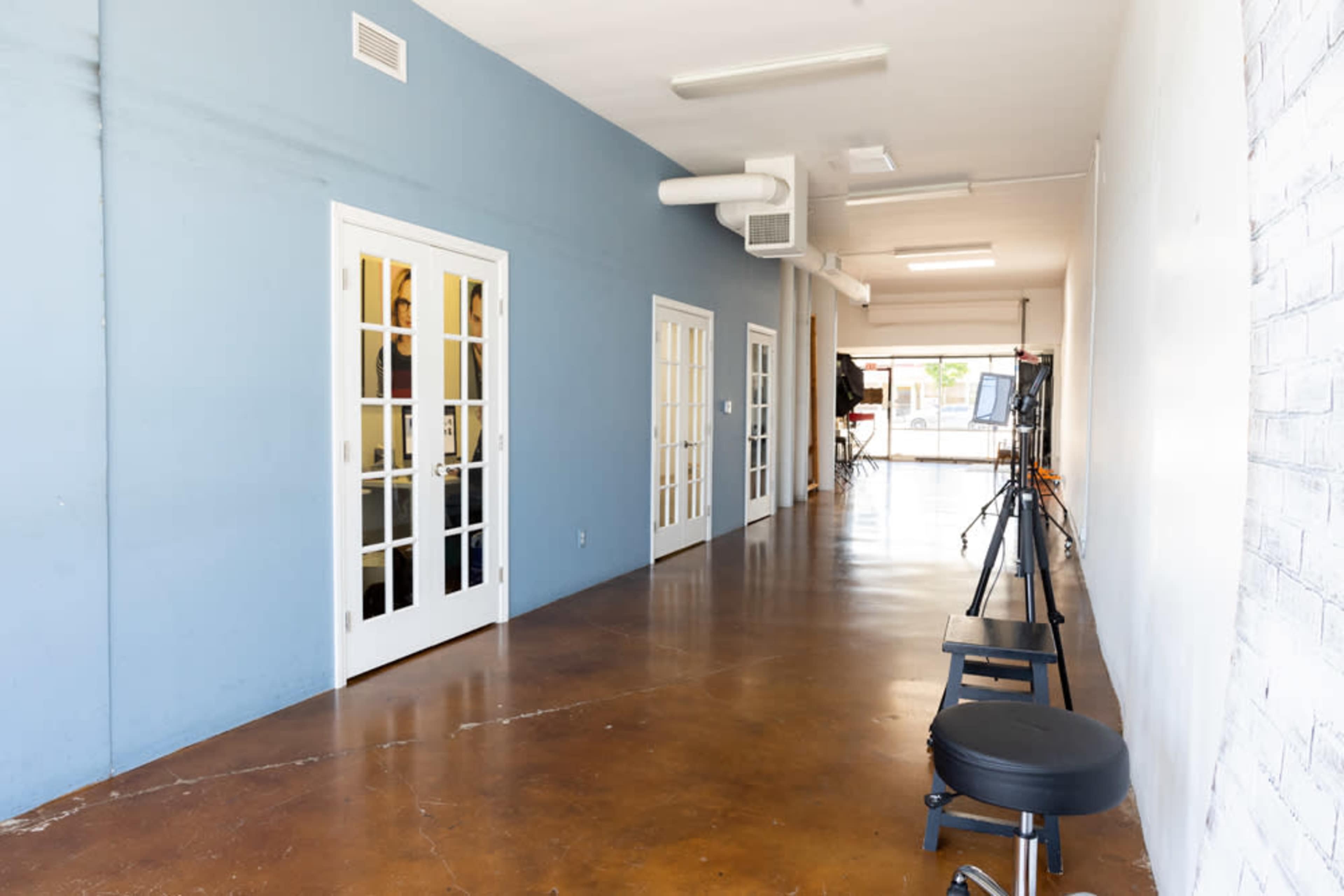 A long hallway with blue walls, featuring several white French doors on one side and a black stool positioned against the wall.