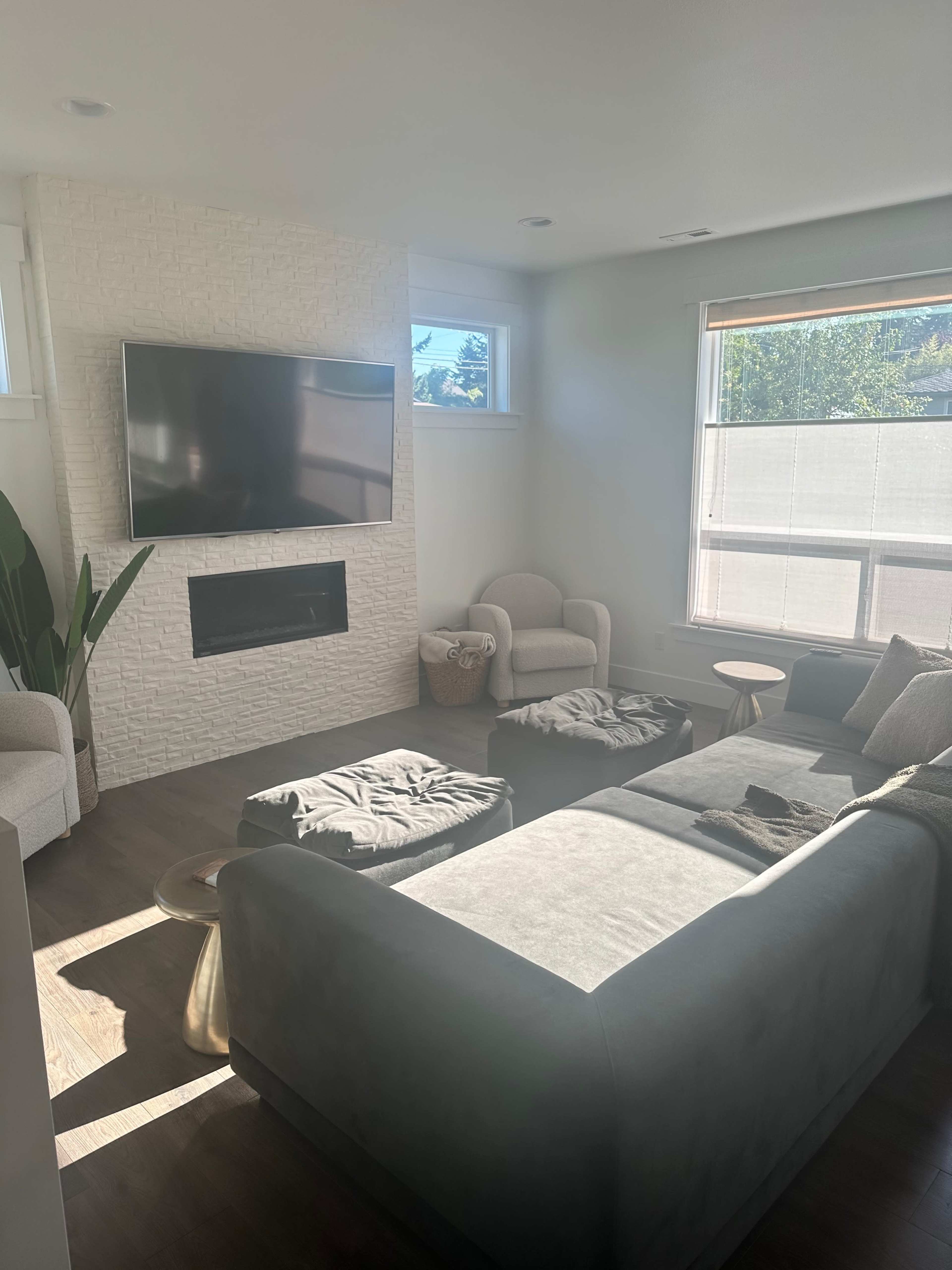 A modern living room features a gray sectional sofa, two armchairs, a wall-mounted TV, and a stone fireplace.
