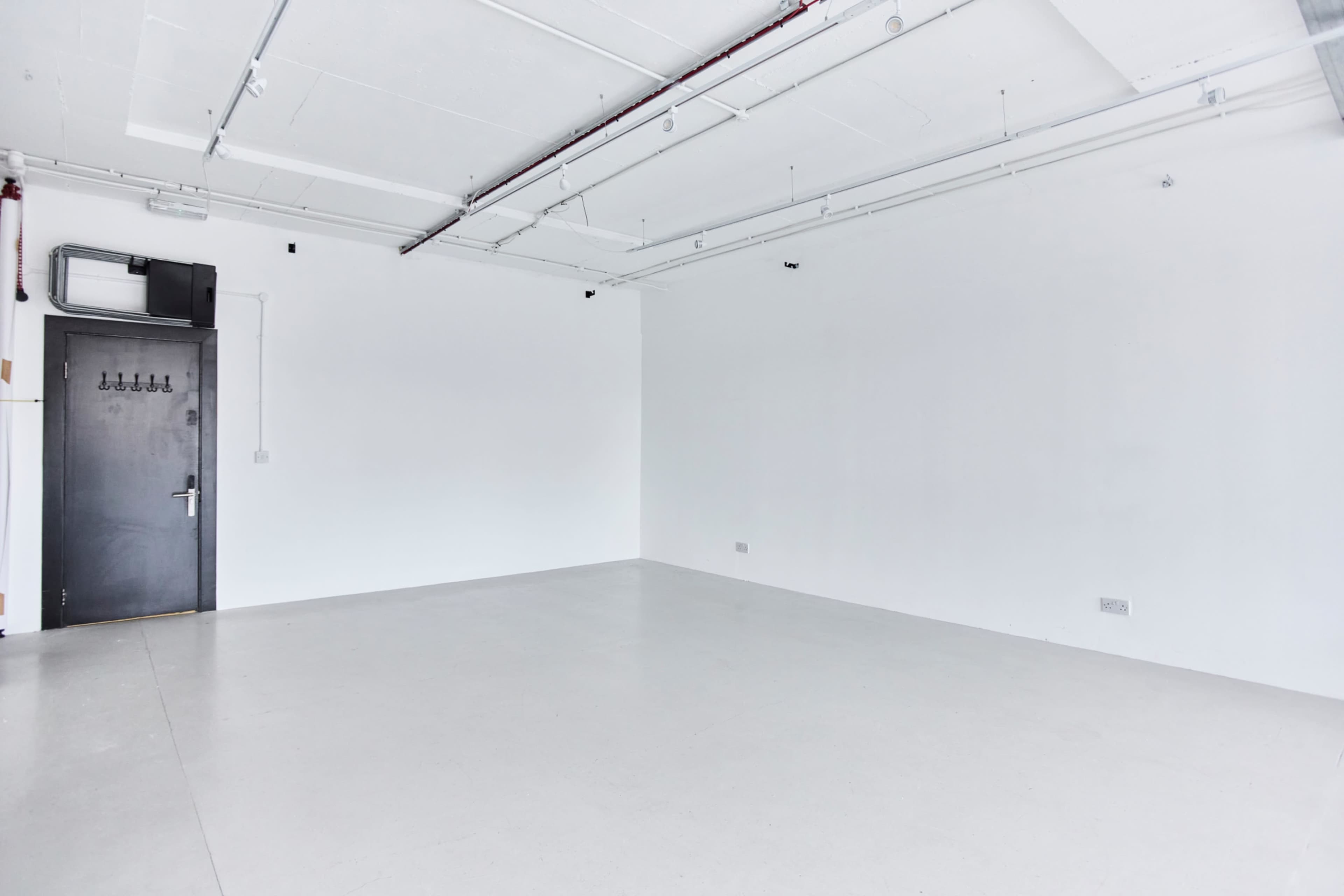 The image shows a spacious, empty room with plain white walls and a concrete floor.