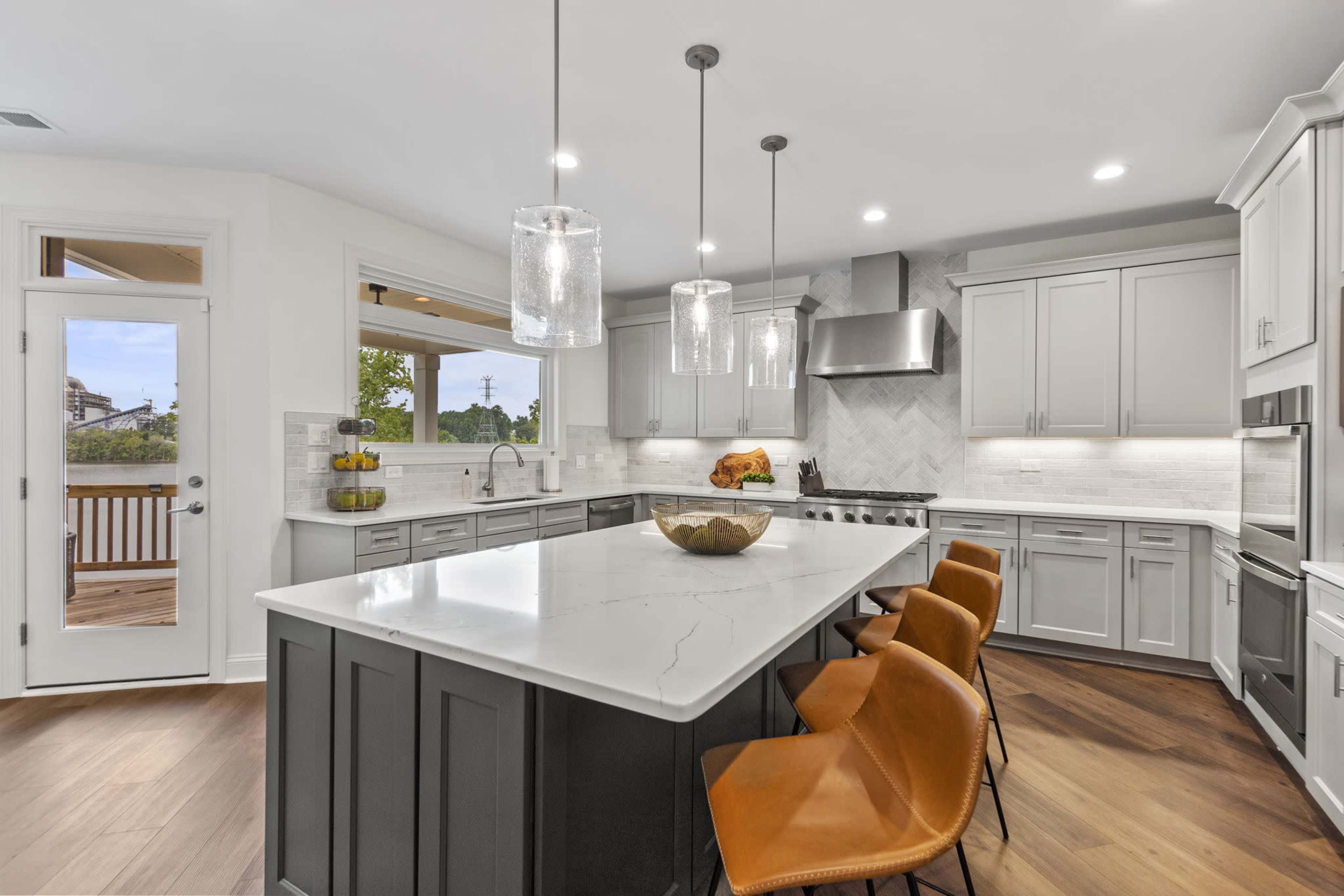 A modern kitchen features a large island with seating, stainless steel appliances, and pendant lighting.