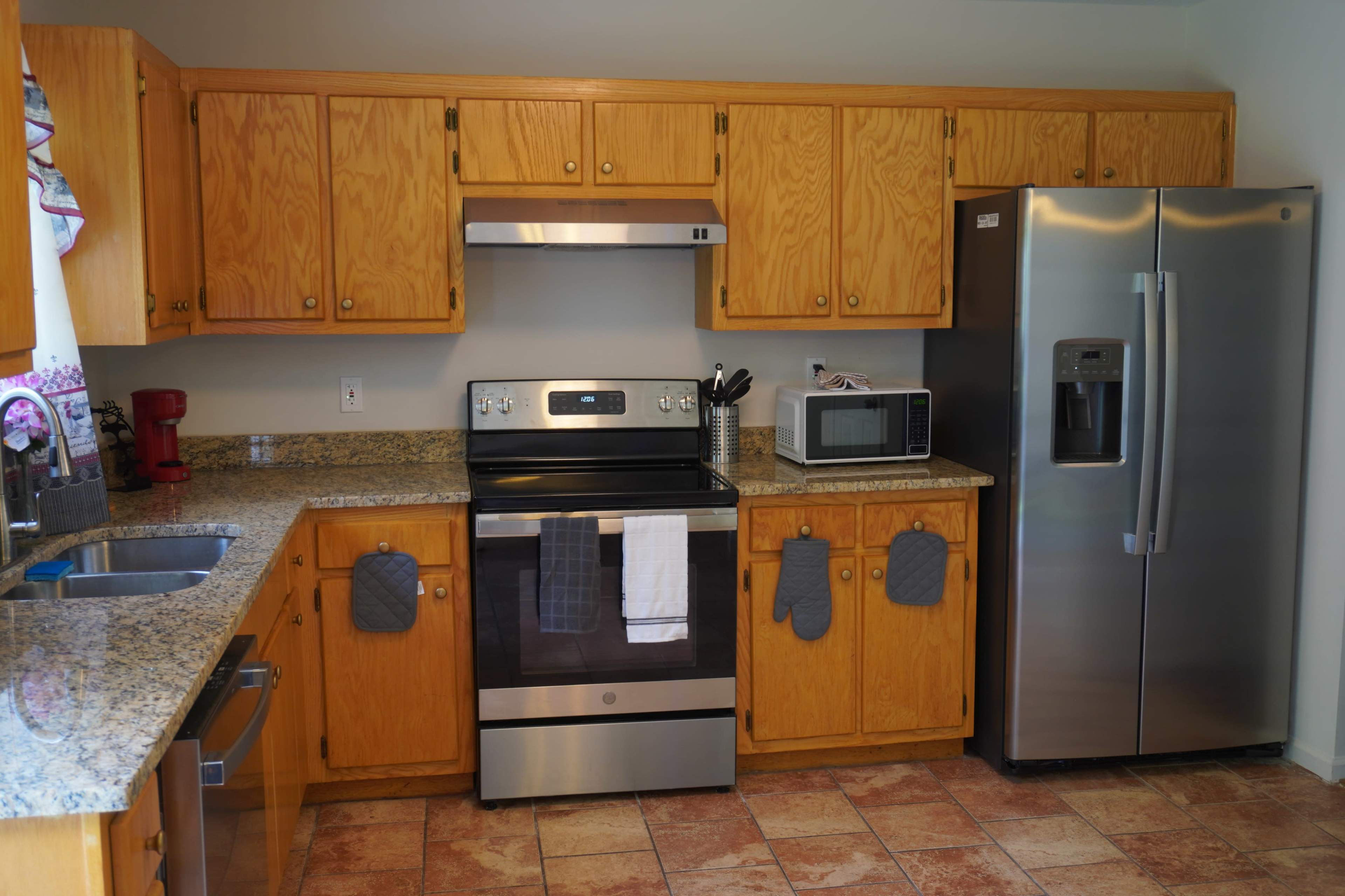 A kitchen with wooden cabinets, a stainless steel refrigerator, an oven, a microwave, and granite countertops.