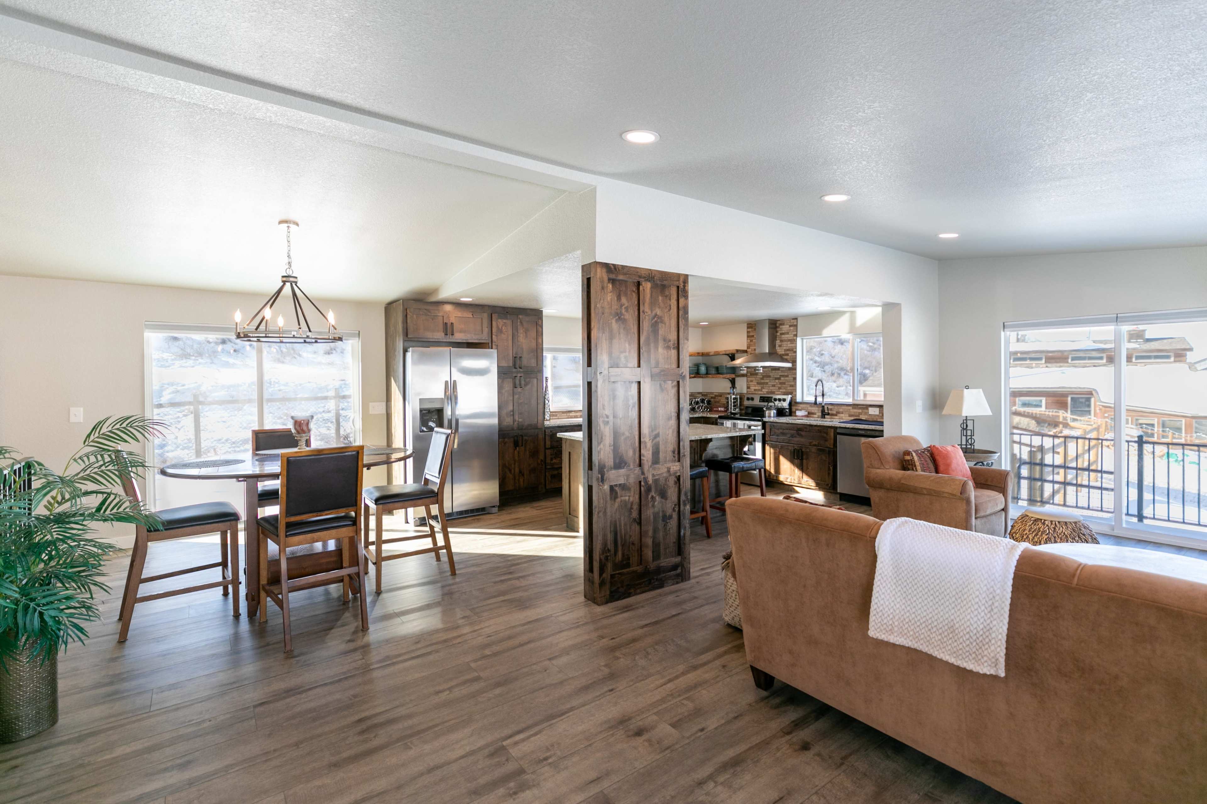 A bright, modern open-concept living space featuring a kitchen, dining area, and living room with large windows offering a view.