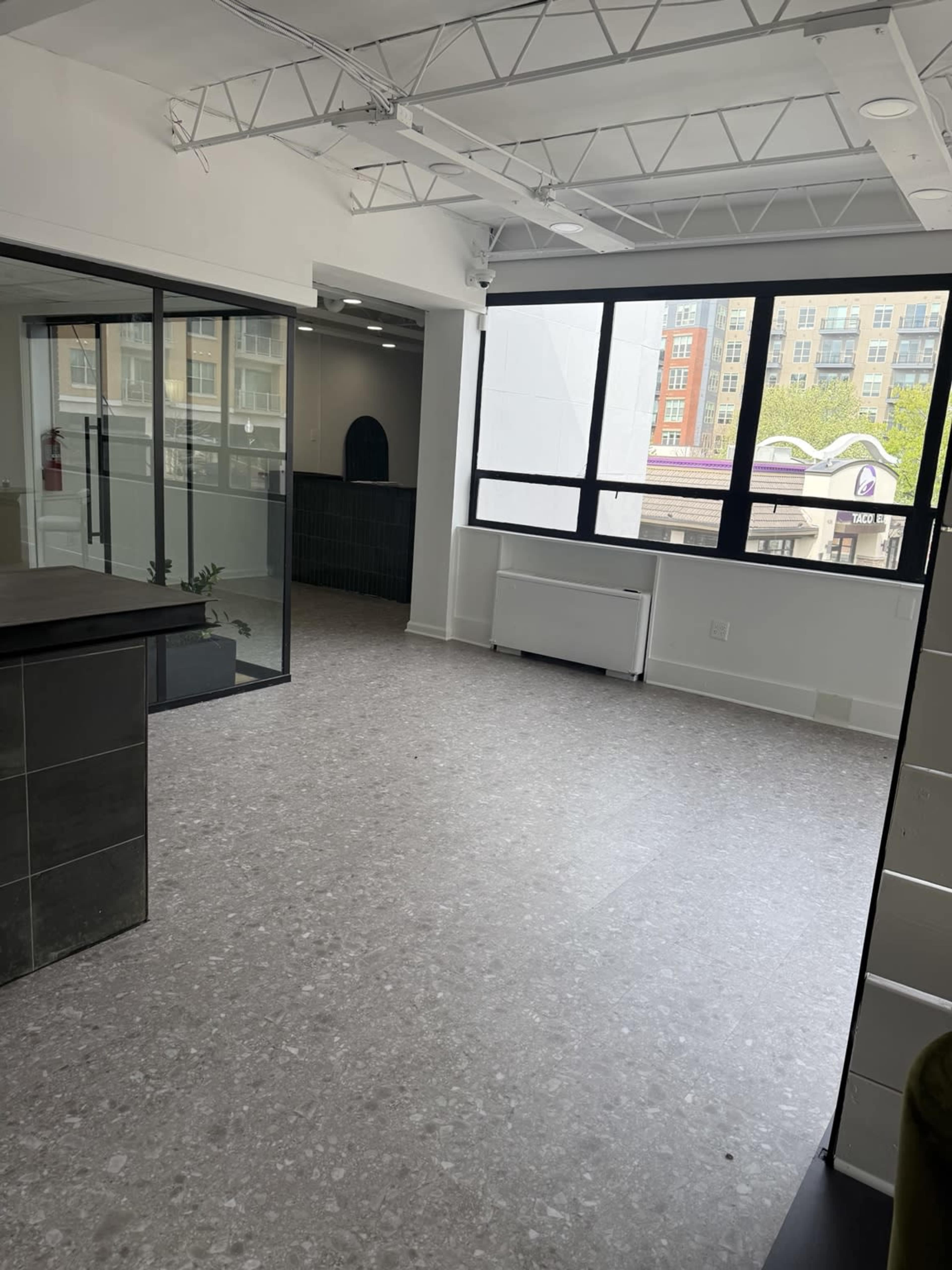 The image shows a modern, empty office space with large windows, polished flooring, and a partitioned area.
