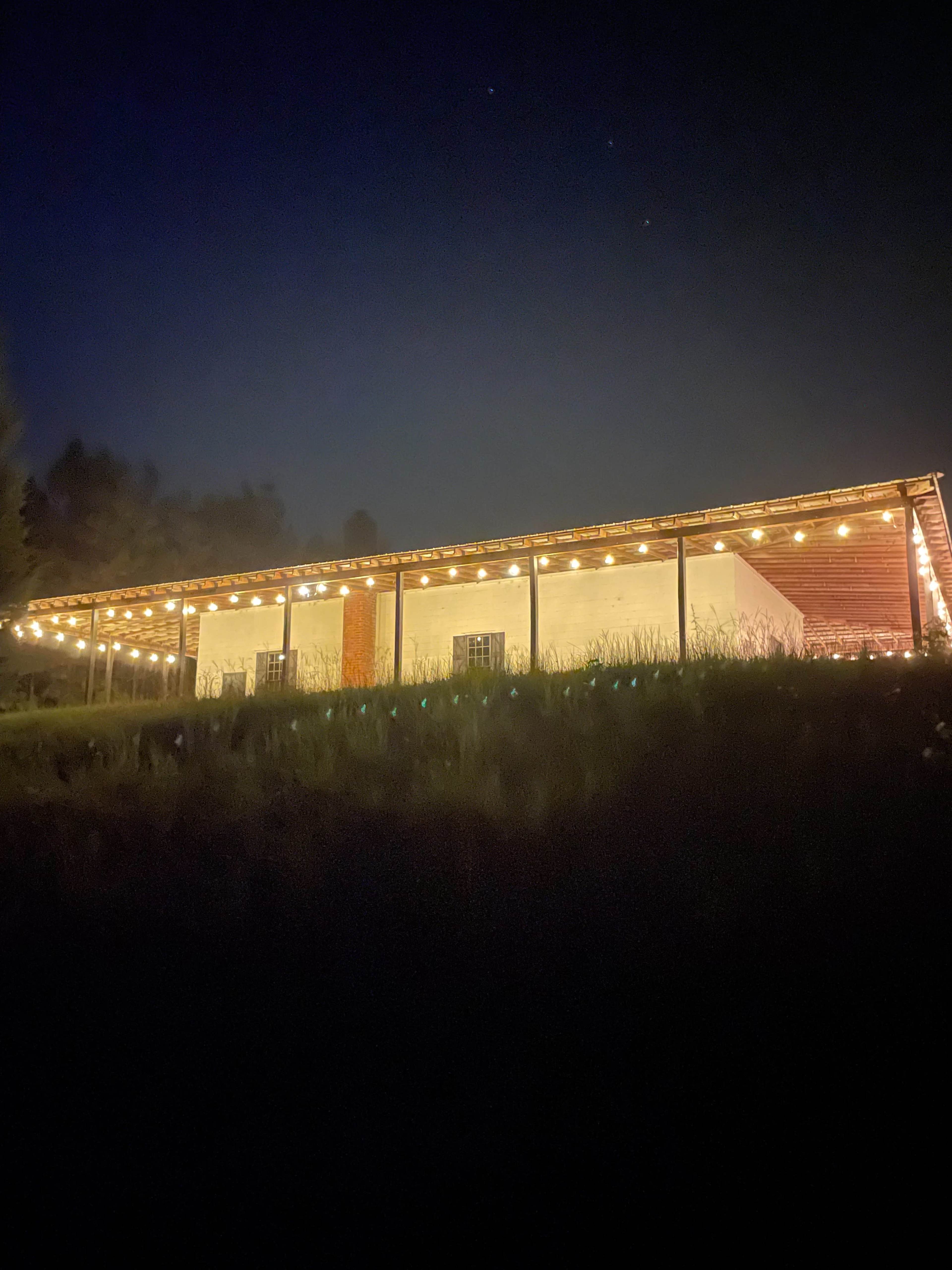 A building is illuminated by string lights at night, with a grassy area in the foreground.
