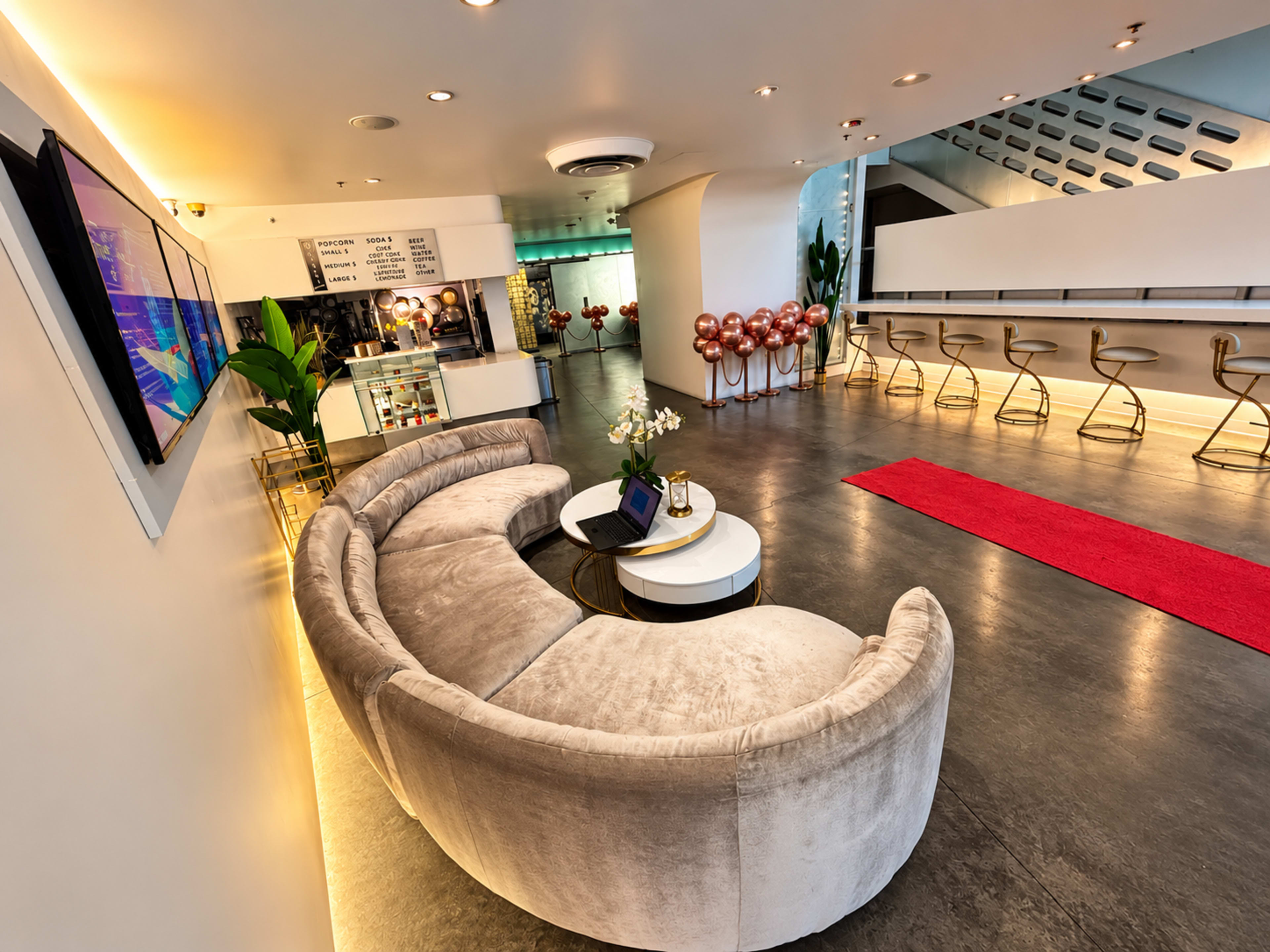 The image shows a modern reception area featuring a curved beige sofa, a coffee table, a small bouquet of flowers, and a long counter with bar stools.
