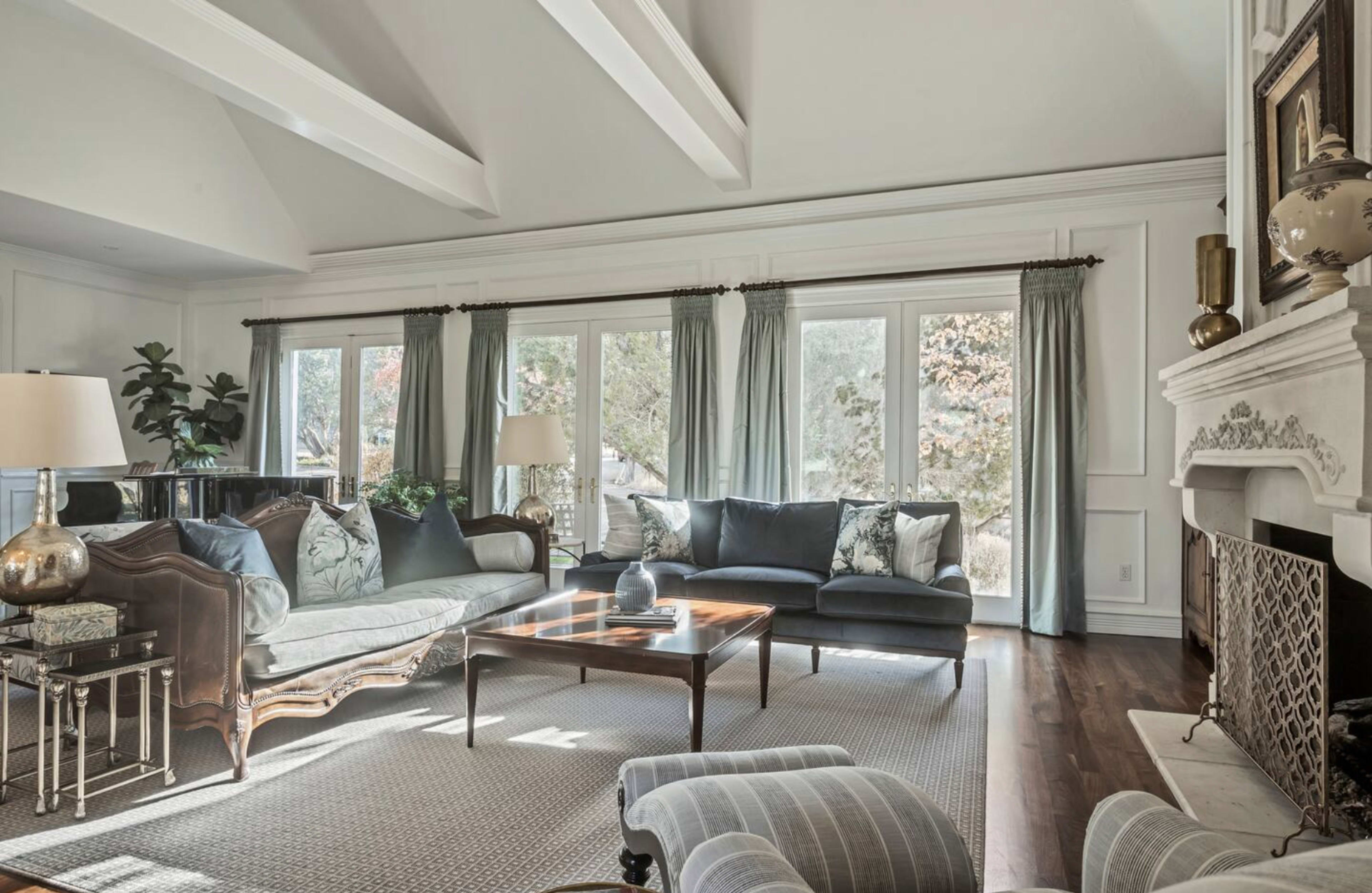 A spacious living room features large windows, a sofa set, and a decorative fireplace.