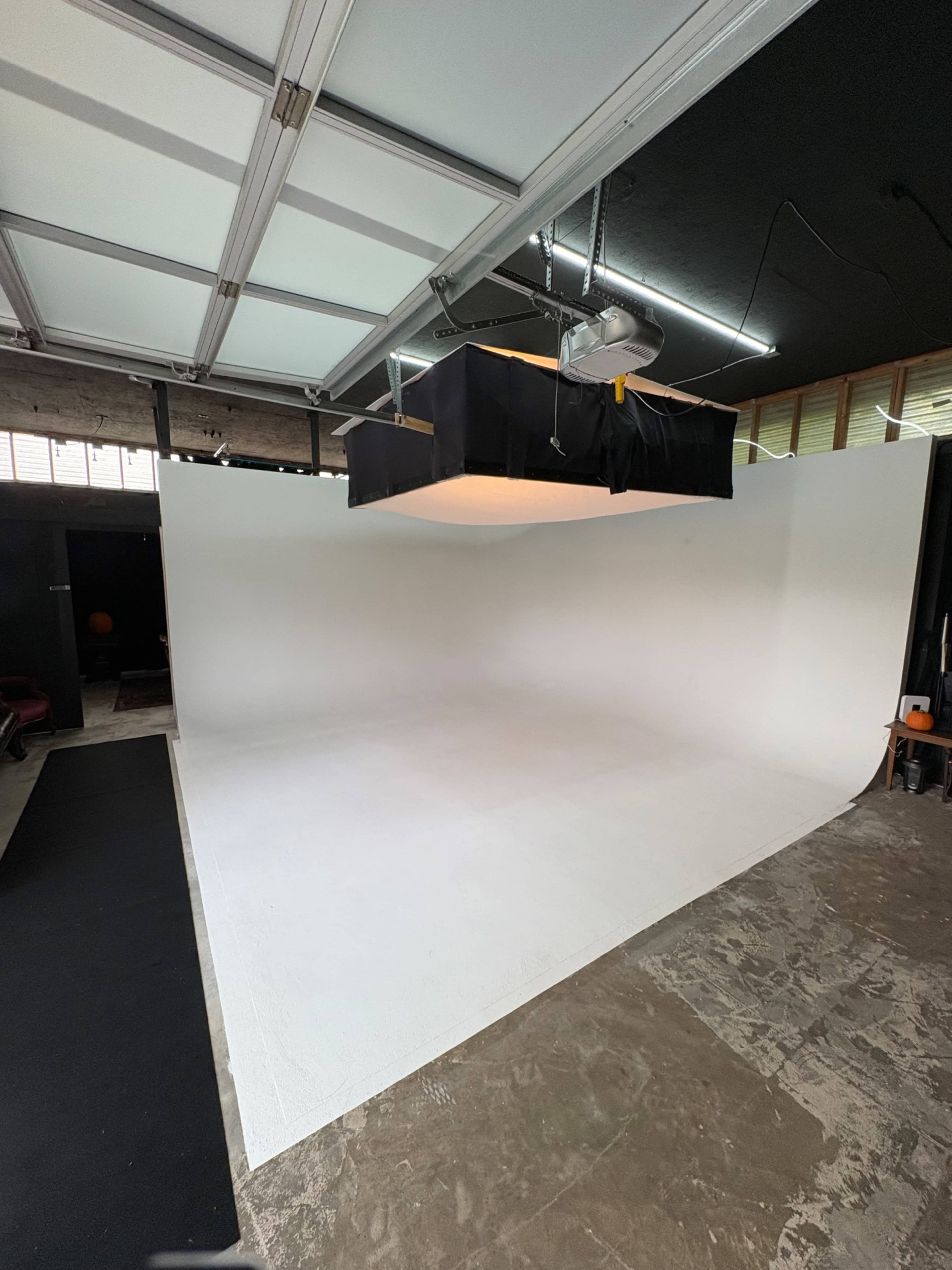 The image shows a spacious photography studio with a curved white backdrop and a softbox light suspended from the ceiling.
