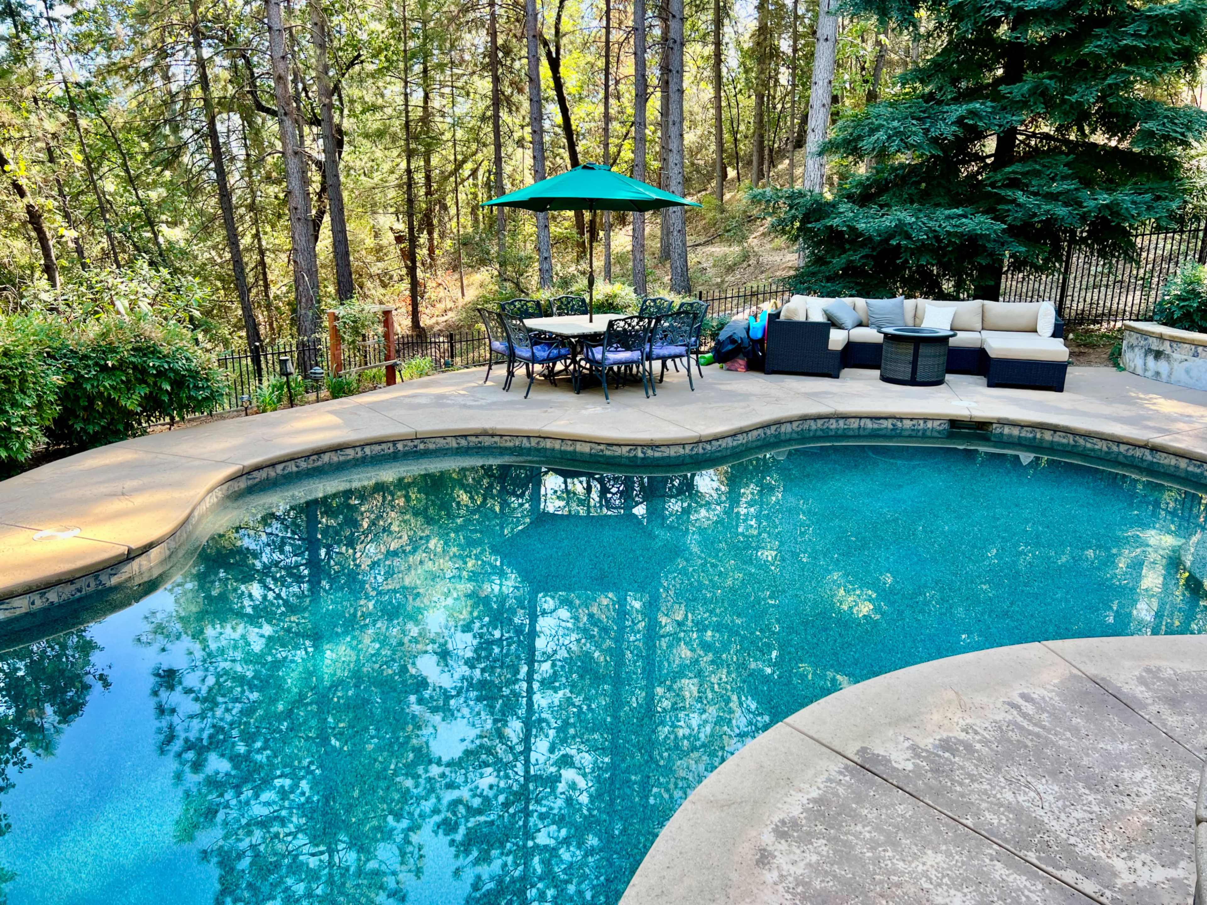 The image shows a swimming pool surrounded by a patio area with outdoor furniture and trees in the background.