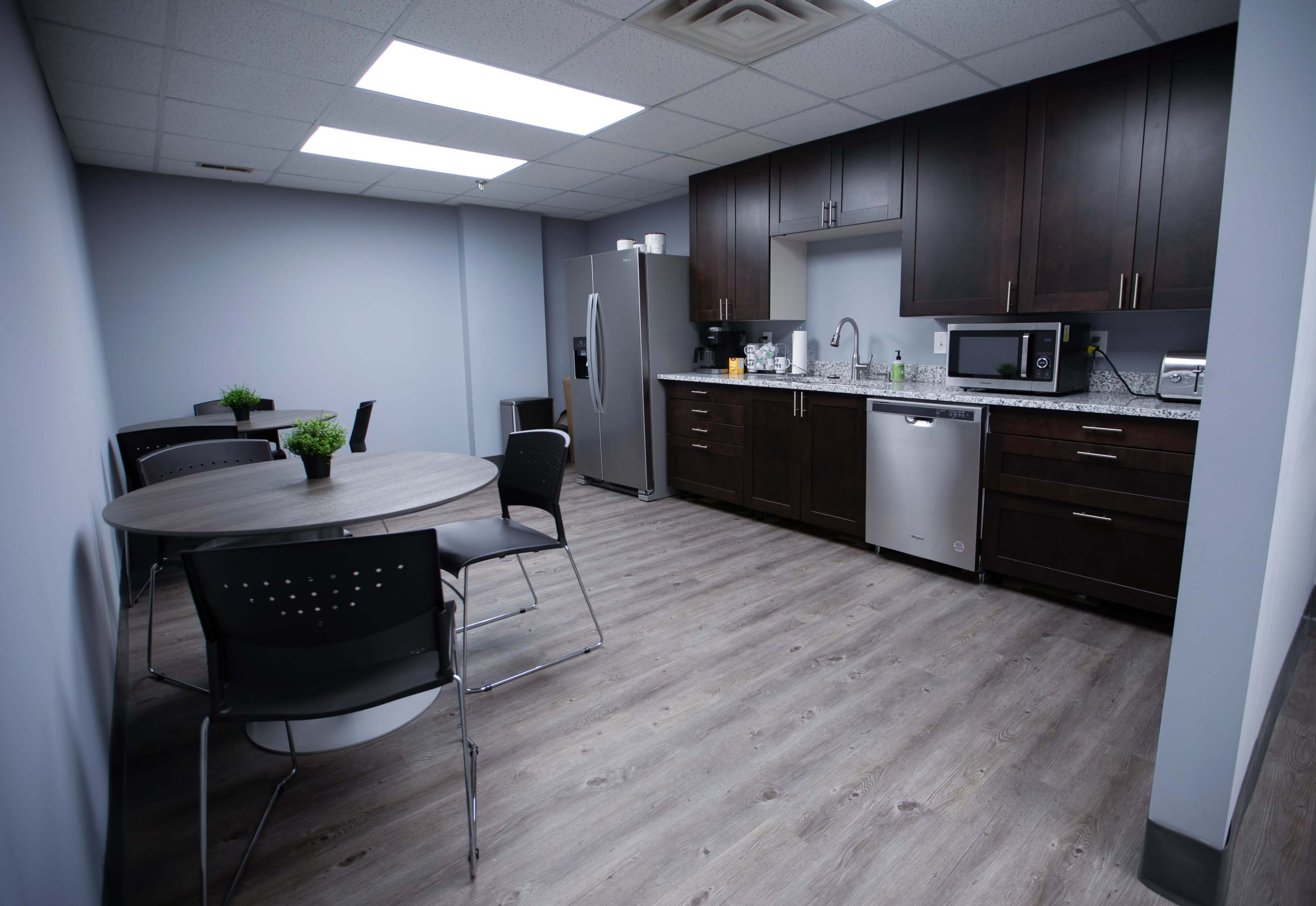 A modern kitchen with dark cabinetry, a stainless steel refrigerator, a microwave, and a dining area featuring a round table and chairs.