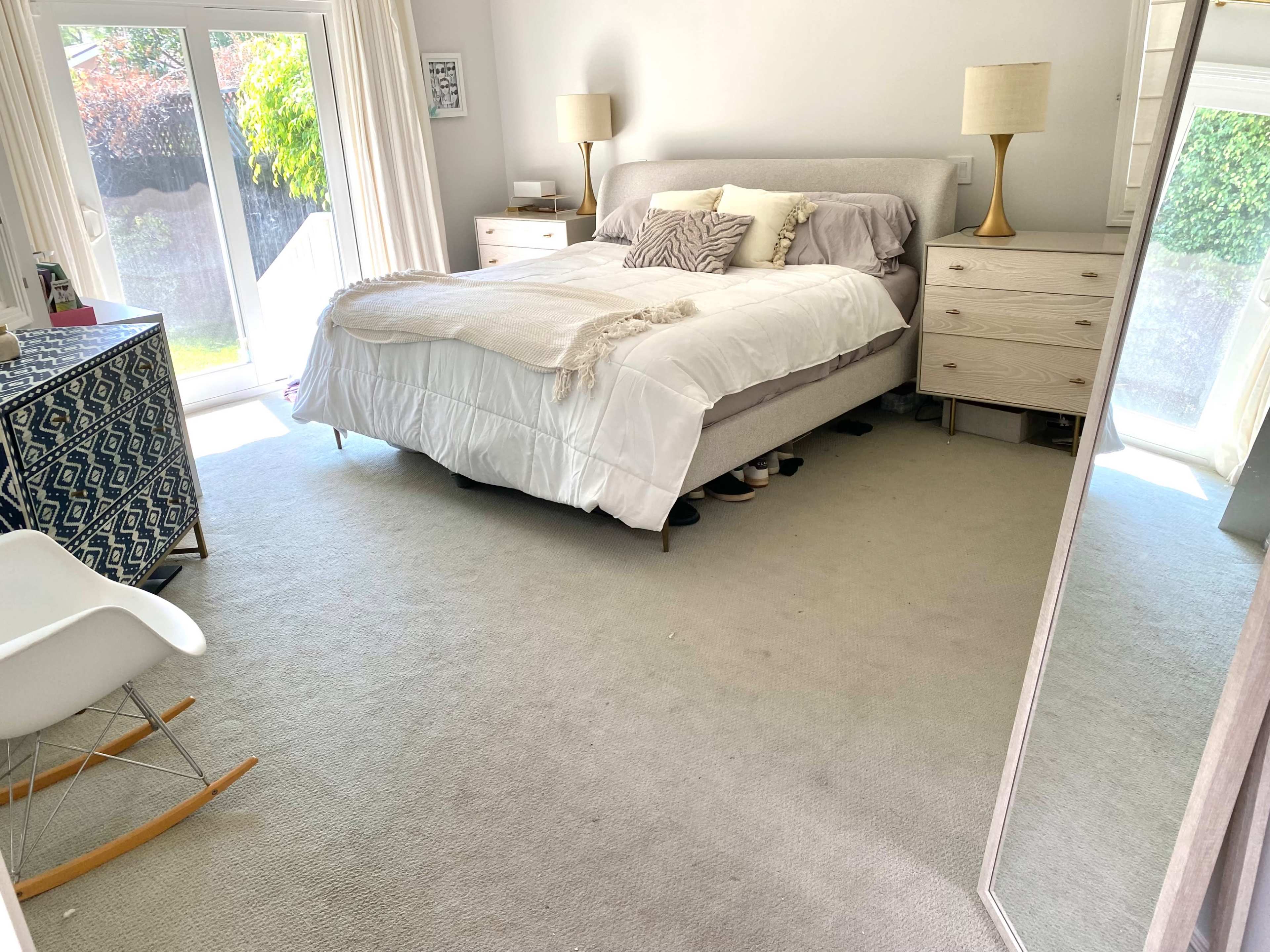 A bedroom with a bed, bedside tables, a dresser, a large mirror, and a sliding glass door leading to an outdoor area.
