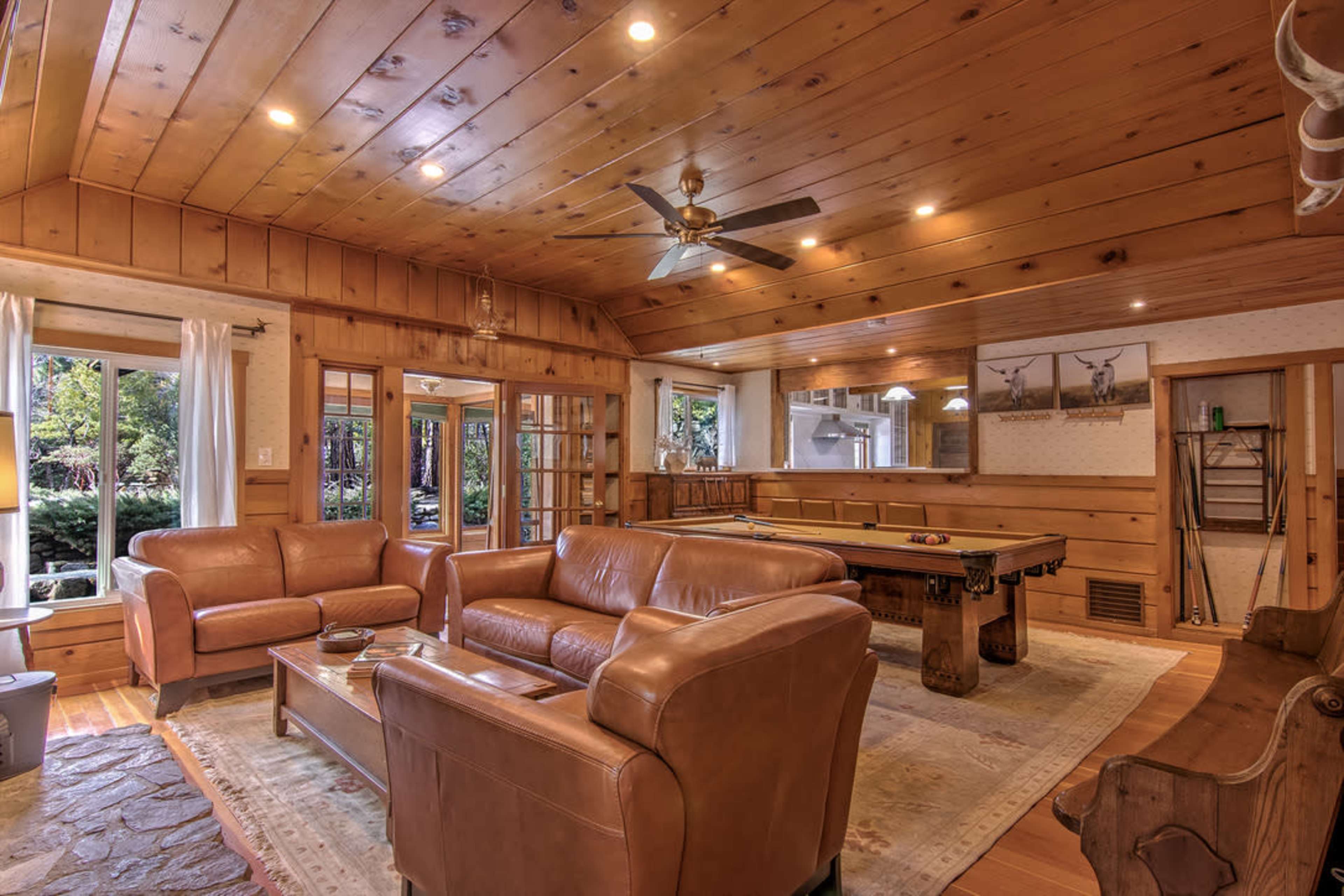 A spacious living room features wooden walls and ceiling, leather couches, and a pool table.