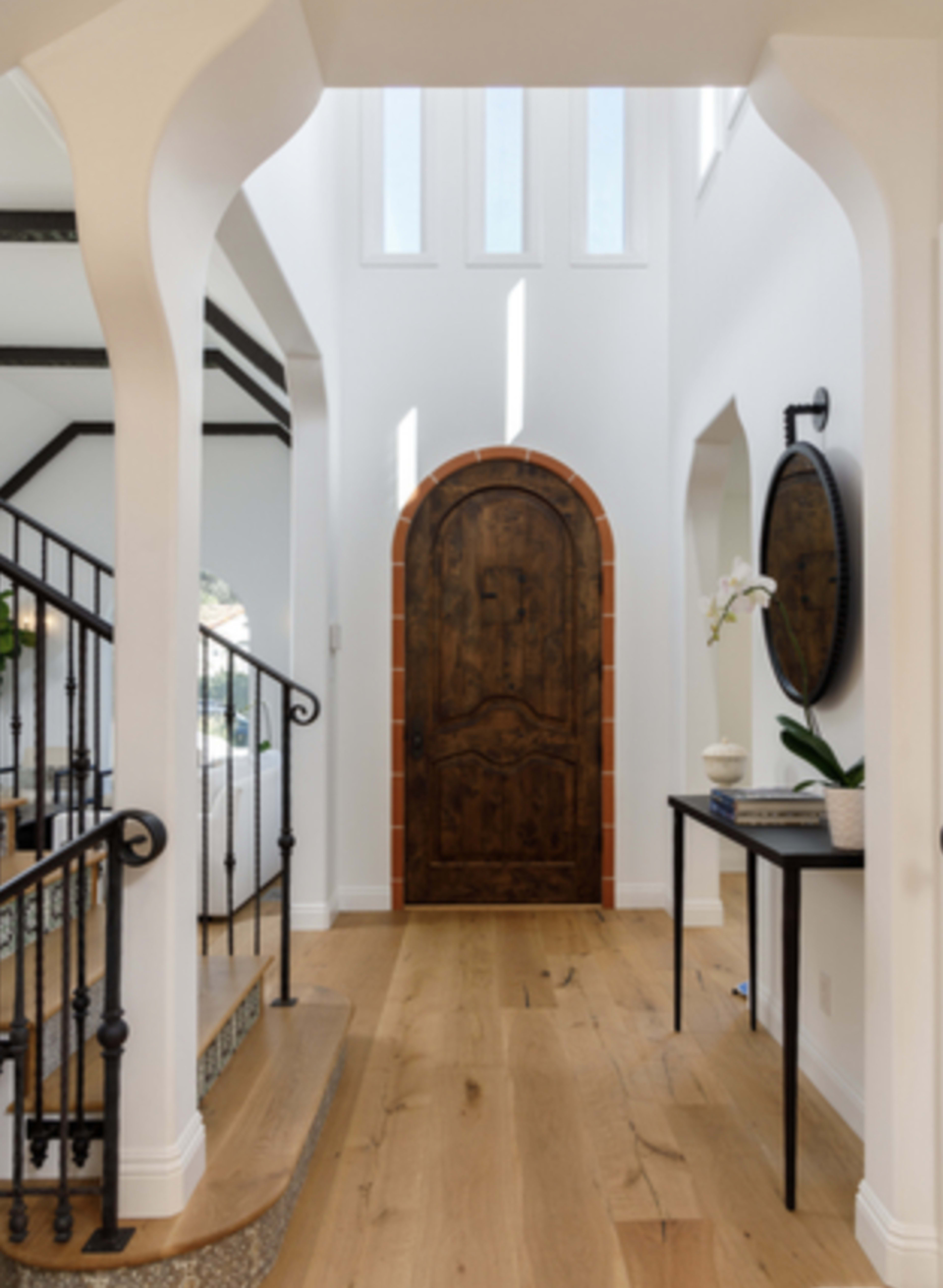 An elegant foyer featuring a curved wooden door, arched entryway, and a decorative staircase with wrought iron railings.