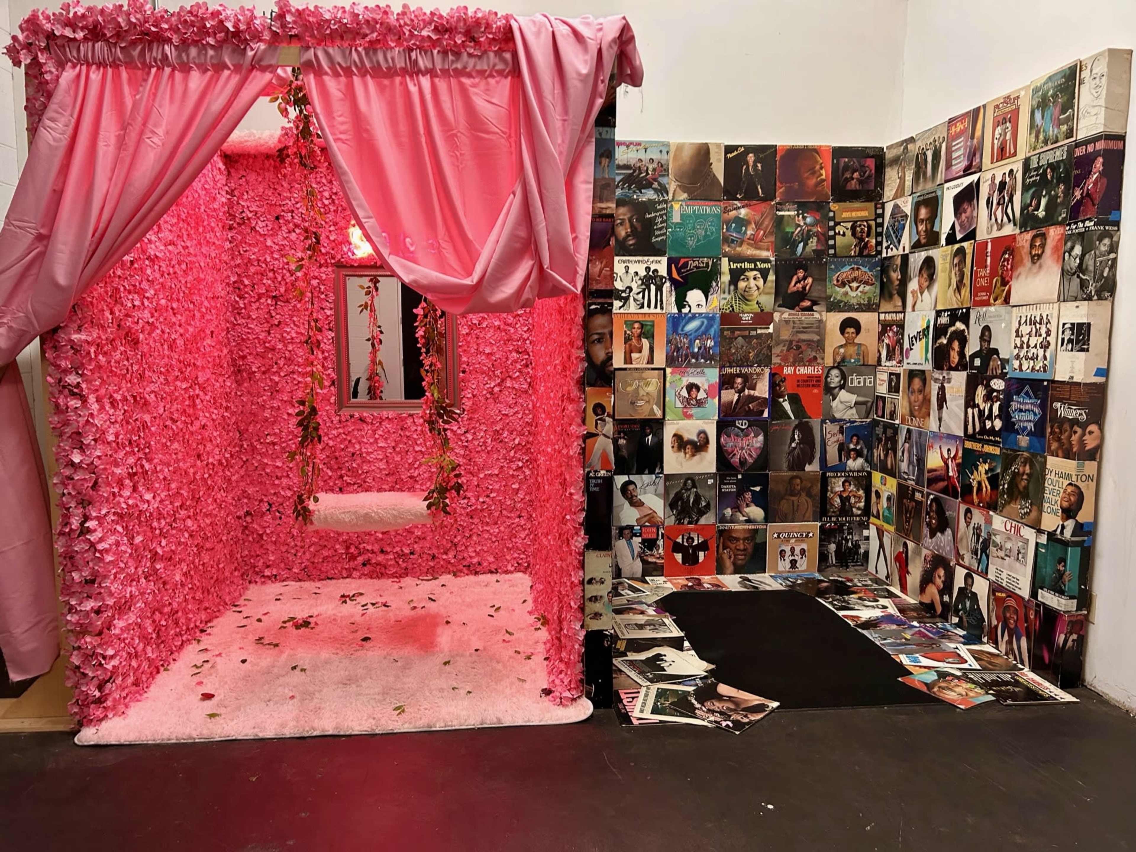 A room decorated with pink floral walls and drapes, featuring a small platform, alongside a wall covered with various vinyl record album covers.
