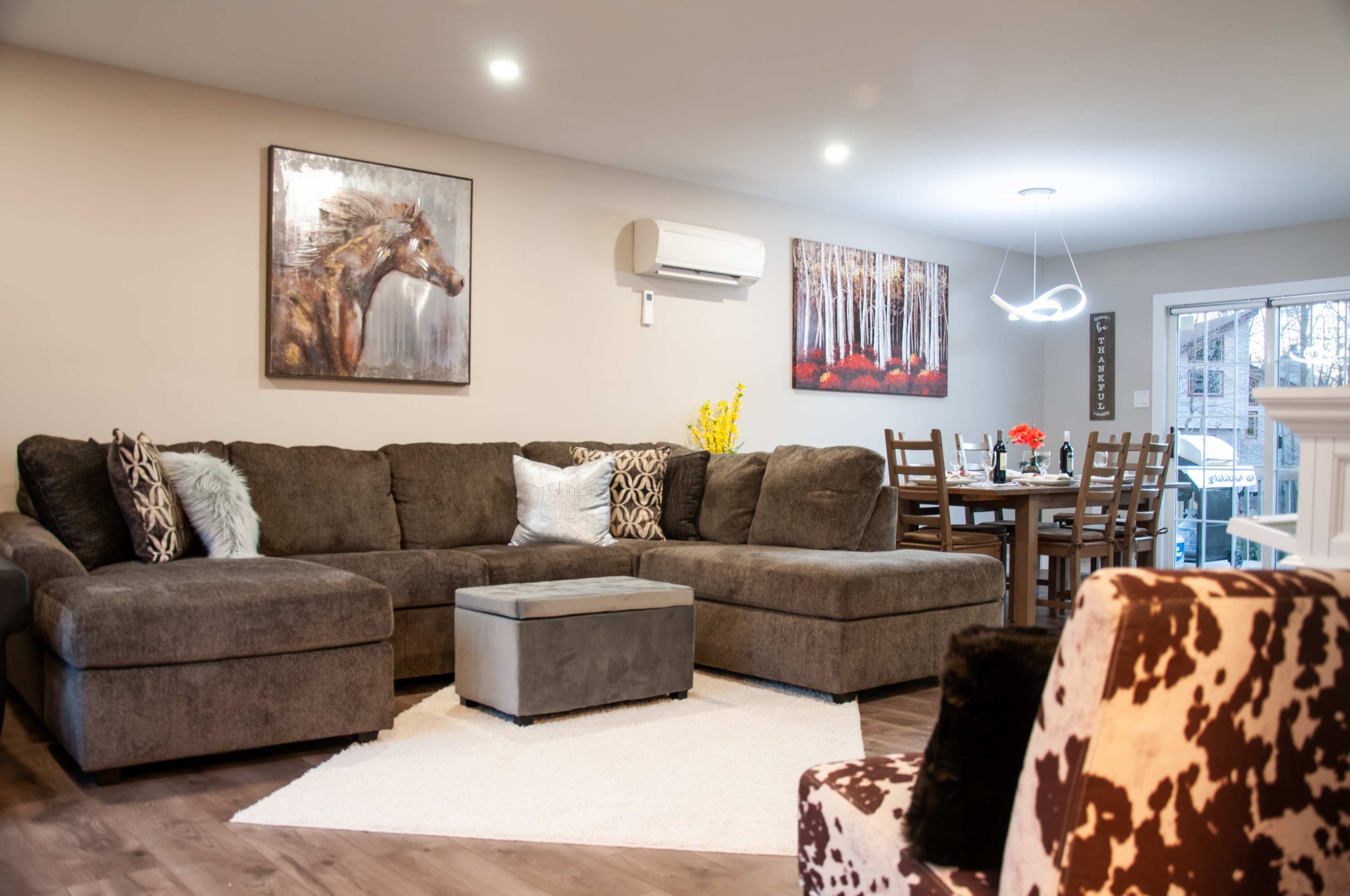 A spacious living room features a large sectional sofa, a coffee table, and artwork on the walls, with a dining area visible in the background.