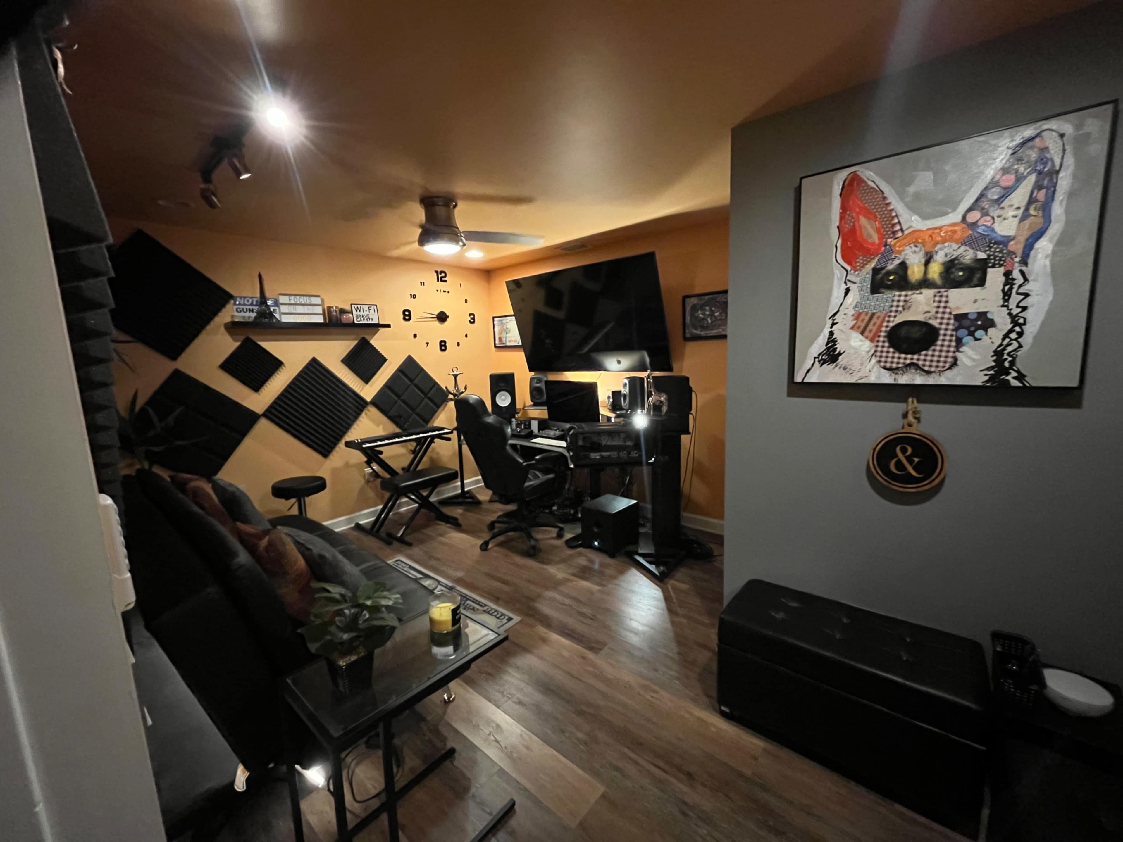 A music studio with soundproofing panels on the walls, a desk with a computer and speakers, and seating areas arranged around a central space.
