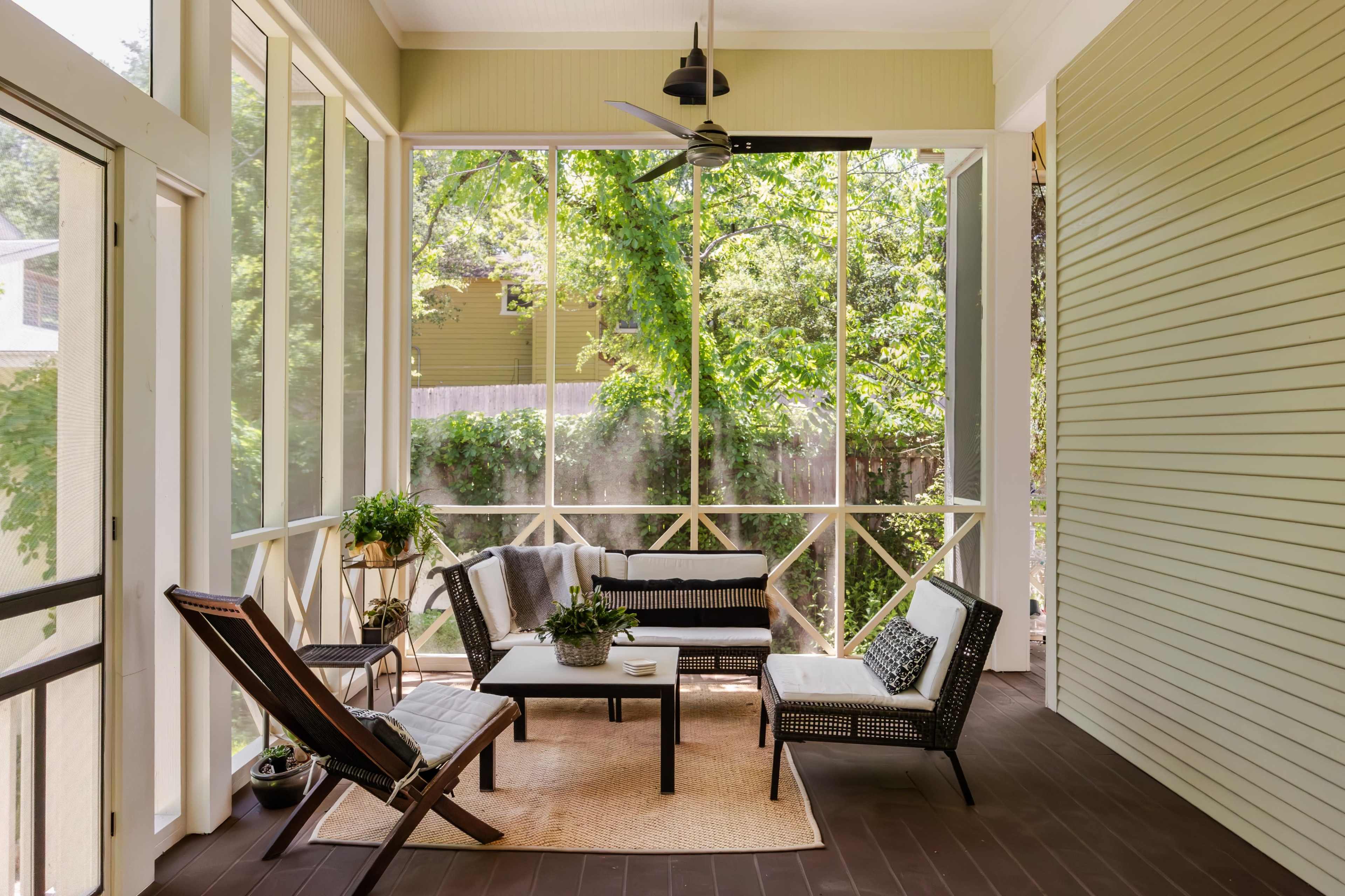 The image shows a screened porch furnished with a table and chairs, a small rug, and greenery visible outside through the screens.